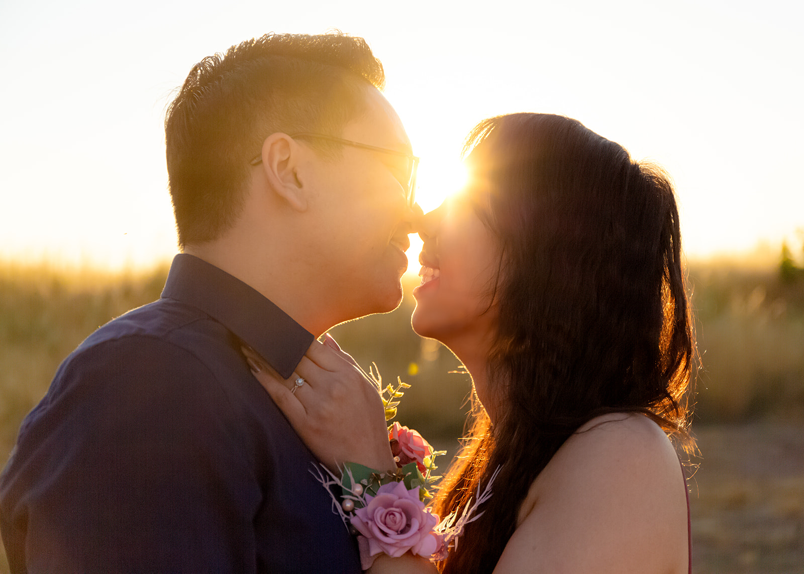 nonbinary person and their girlfriend kissing with sun shining between them at sunrise