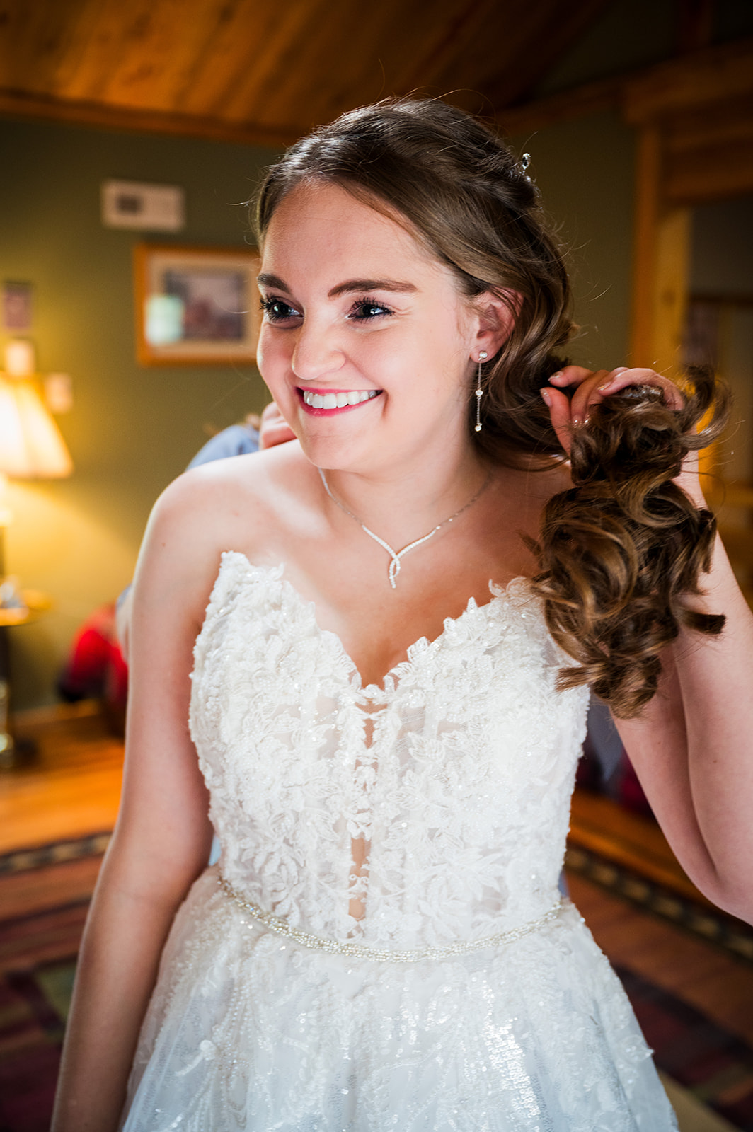 The smiling bride moves her hair so her mother can fasten her necklace.