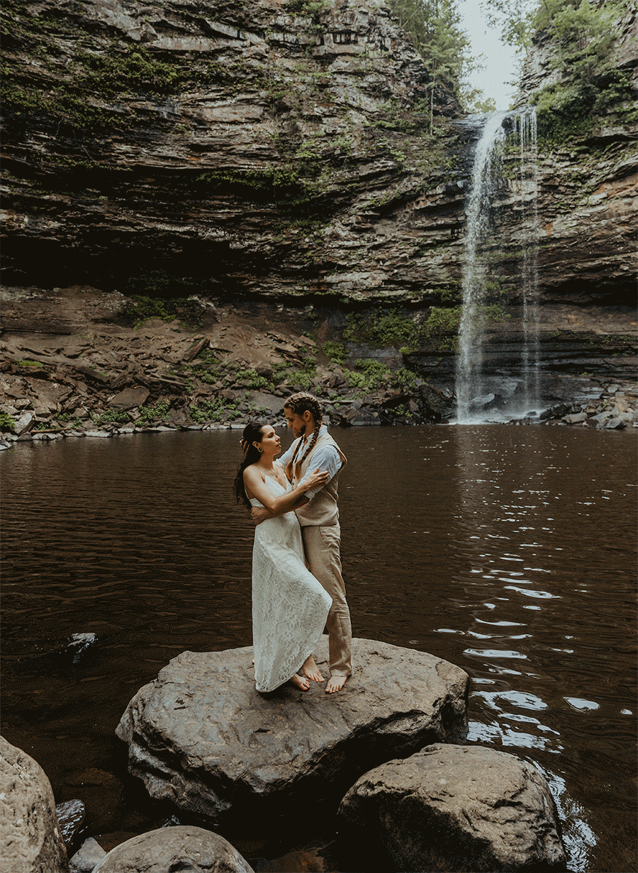 A couple on their elopement day kiss in front of a waterfall
