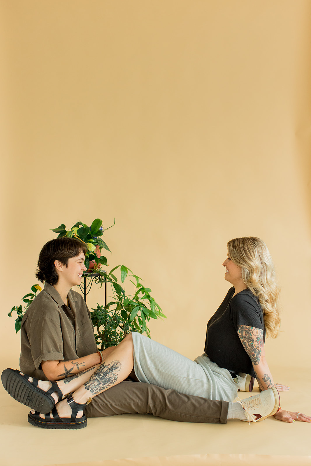 A couple sits on the floor in front of a backdrop with legs draped over each other