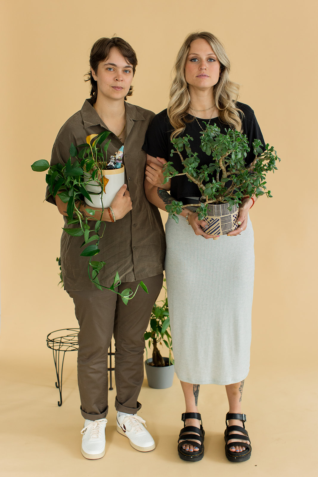 A couple looks at the camera while holding their beloved houseplants for a creative photo