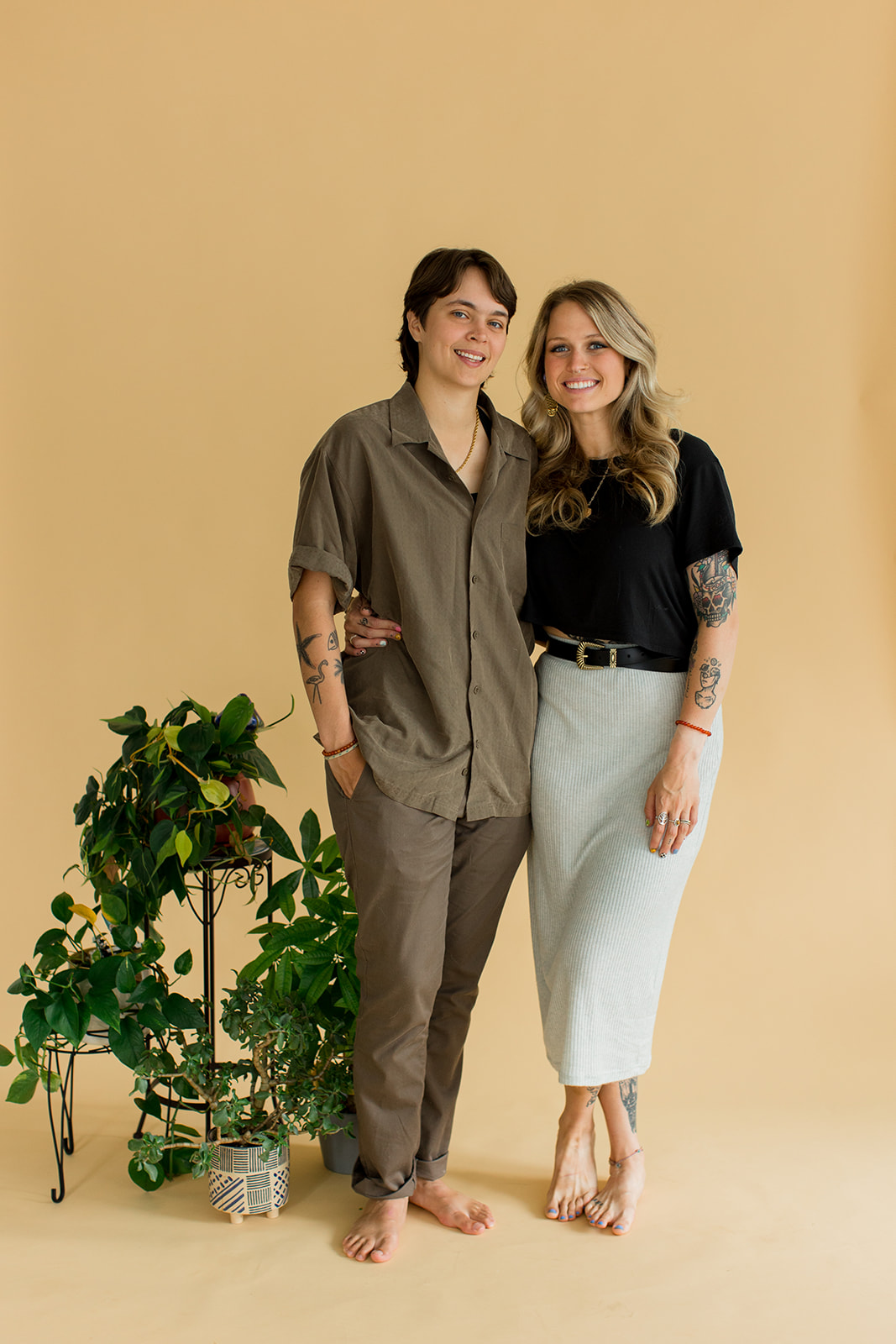 A couple laugh and smile at the camera while standing in front of a backdrop with their beloved houseplants.