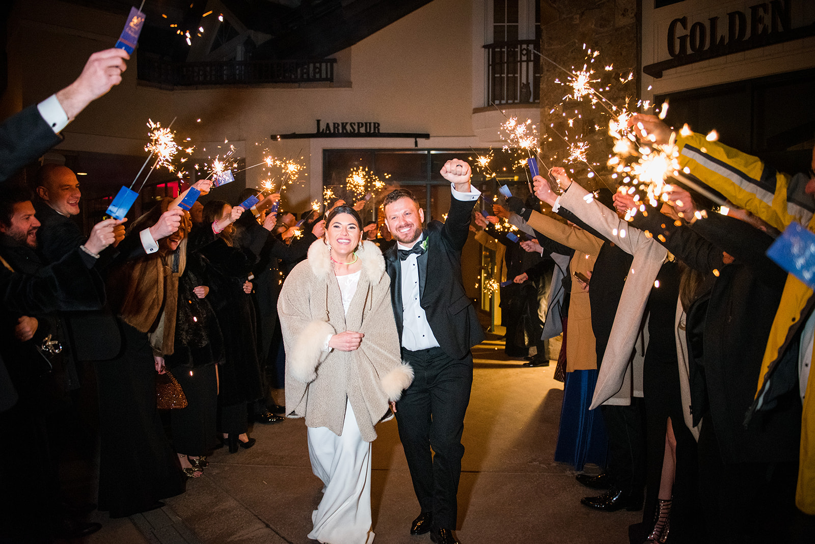 Bride and groom exit their wedding reception surrounded by guests with sparklers.