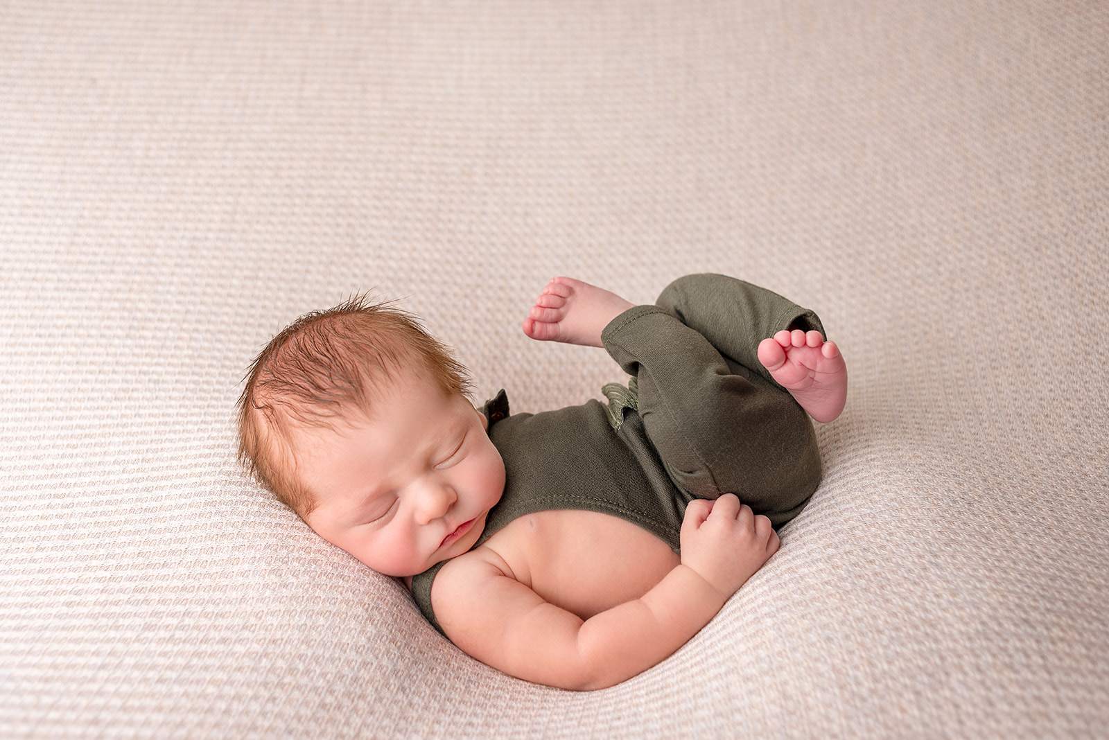 Newborn boy in Celesta Champagne Photography studio in Carthage, Missouri in a green knit romper on a cream blanket