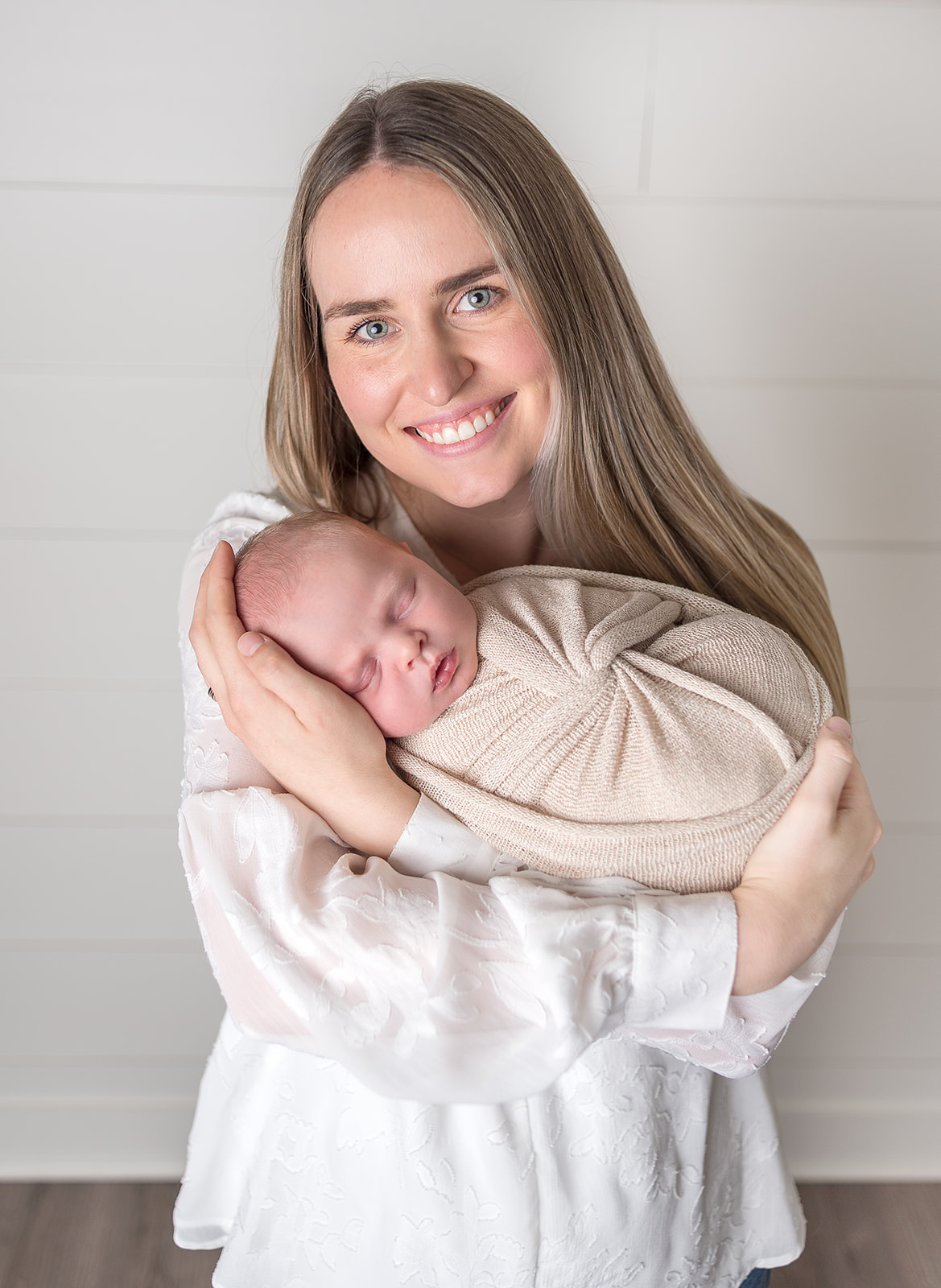 A new mom holding her newborn son in a cream swaddle in a all white backdrop studio in Carthage, Missouri
