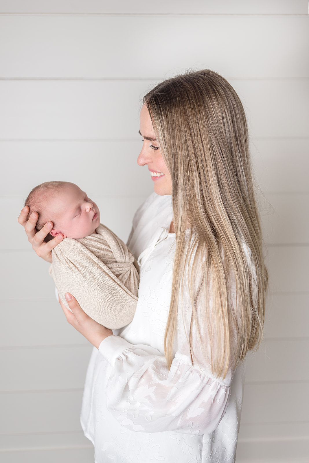 A new mom holding her newborn son in a cream swaddle in a all white backdrop studio in Carthage, Missouri