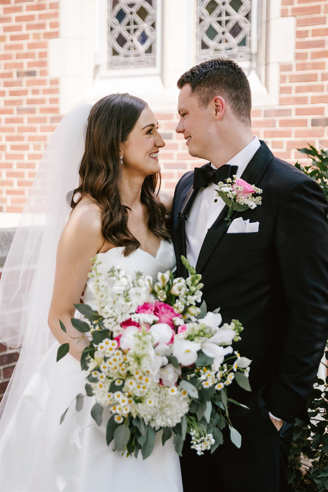 The bride and groom stand in the courtyard, with a bouquet of pink, white, and yellow flowers, creating a vibrant scene.