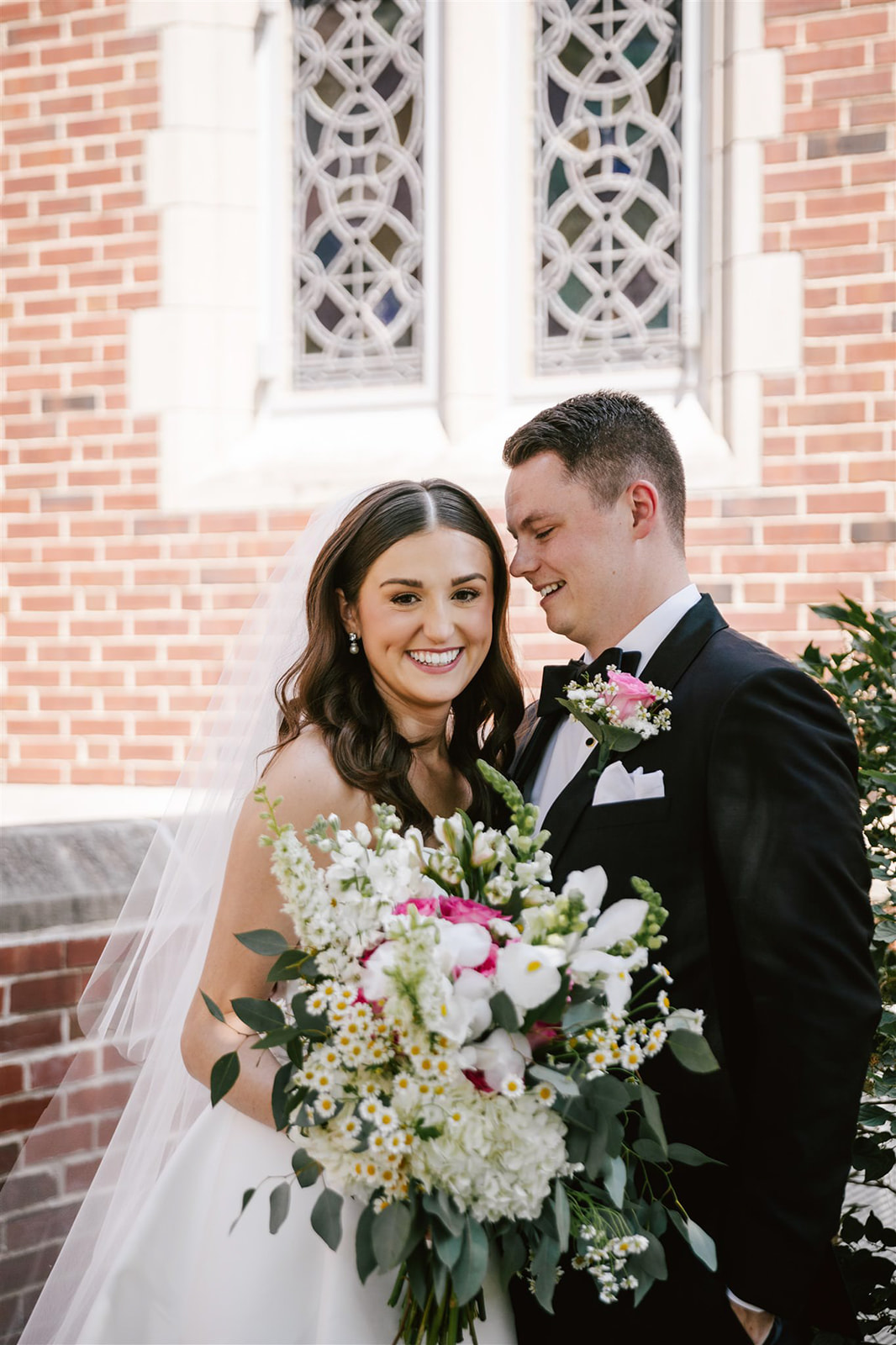 The bride and groom stand in the courtyard, with a bouquet of pink, white, and yellow flowers, creating a vibrant scene.