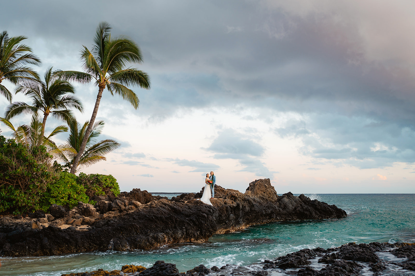 A couple enjoys sunset on the black lava rocks at Makena Cove during their Maui Elopement with photographer Colby Moore