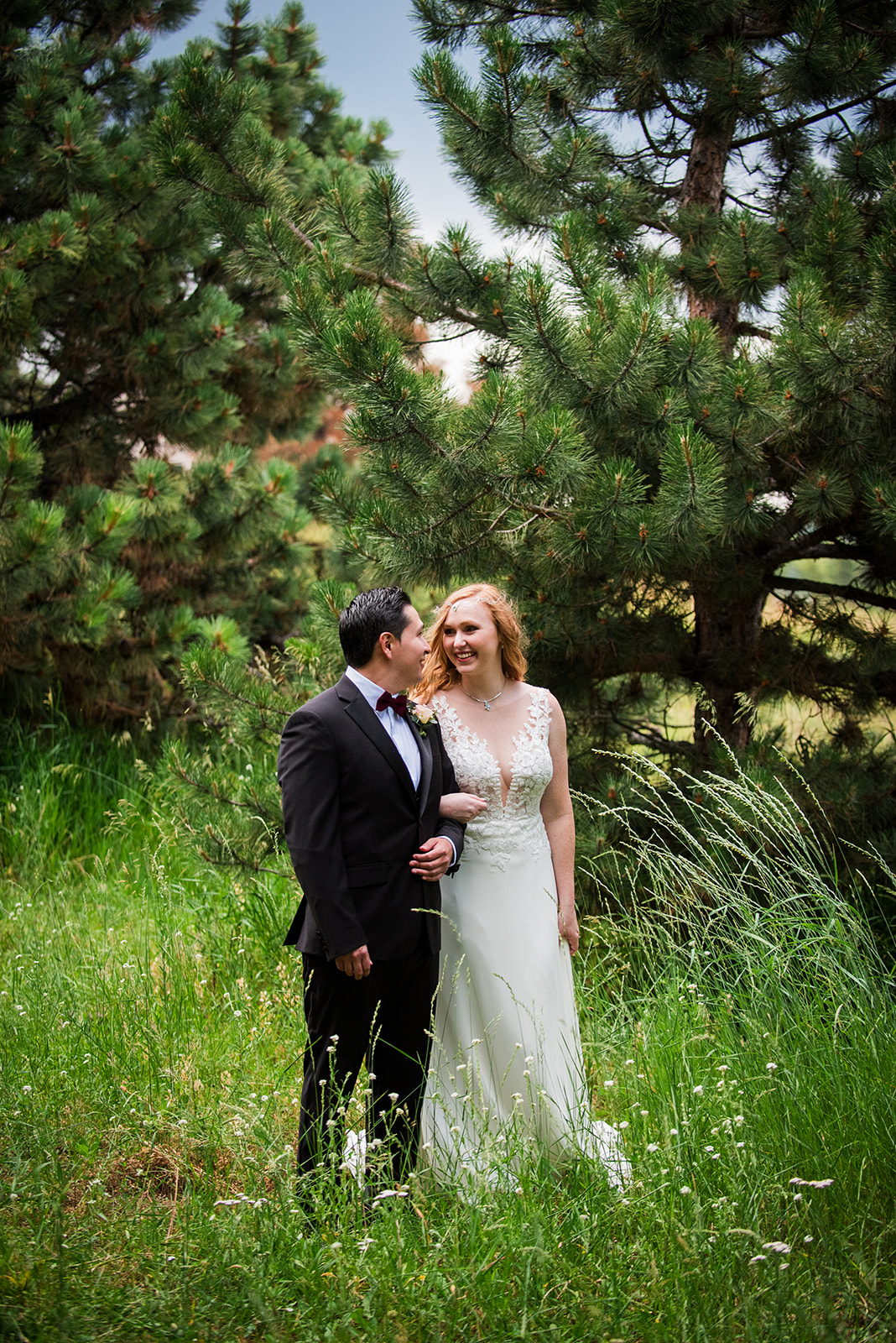 The bride and groom stand arm in arm in a green wooded area.