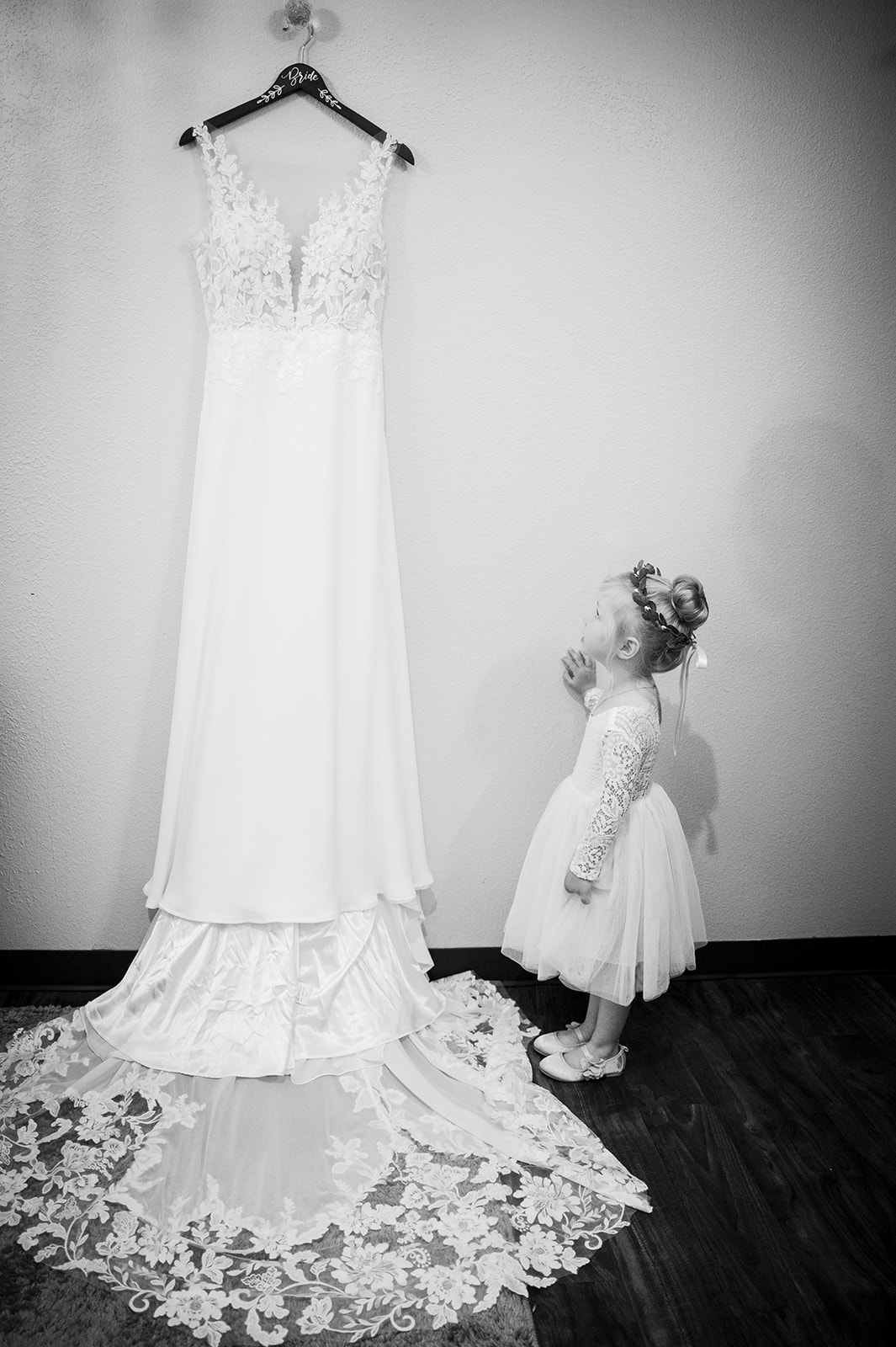 The little flower girl looks up at the hanging wedding dress.