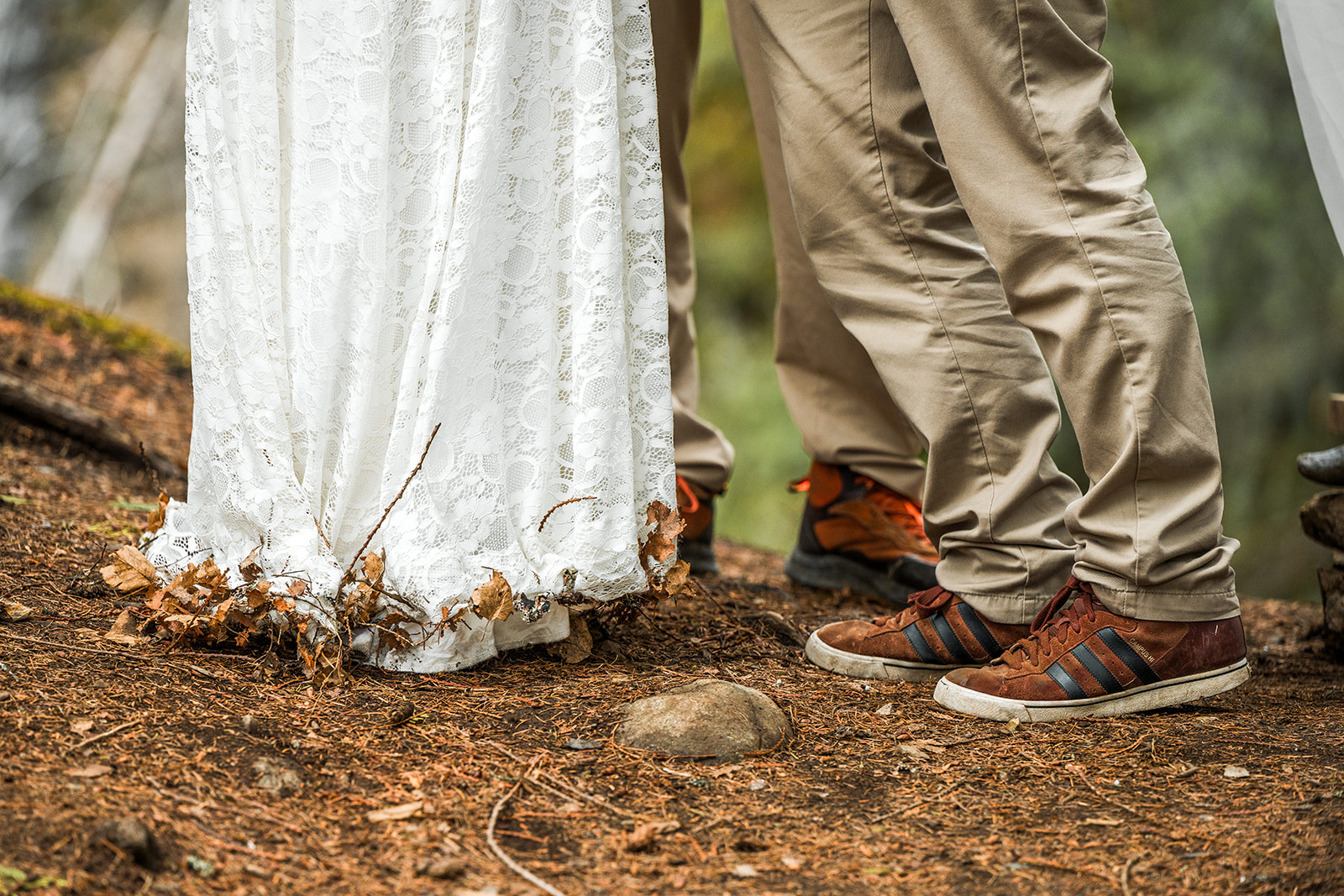a closeup of the groom's shoes and the hem of the bride's dress, thickly matted with debris from the forest floor