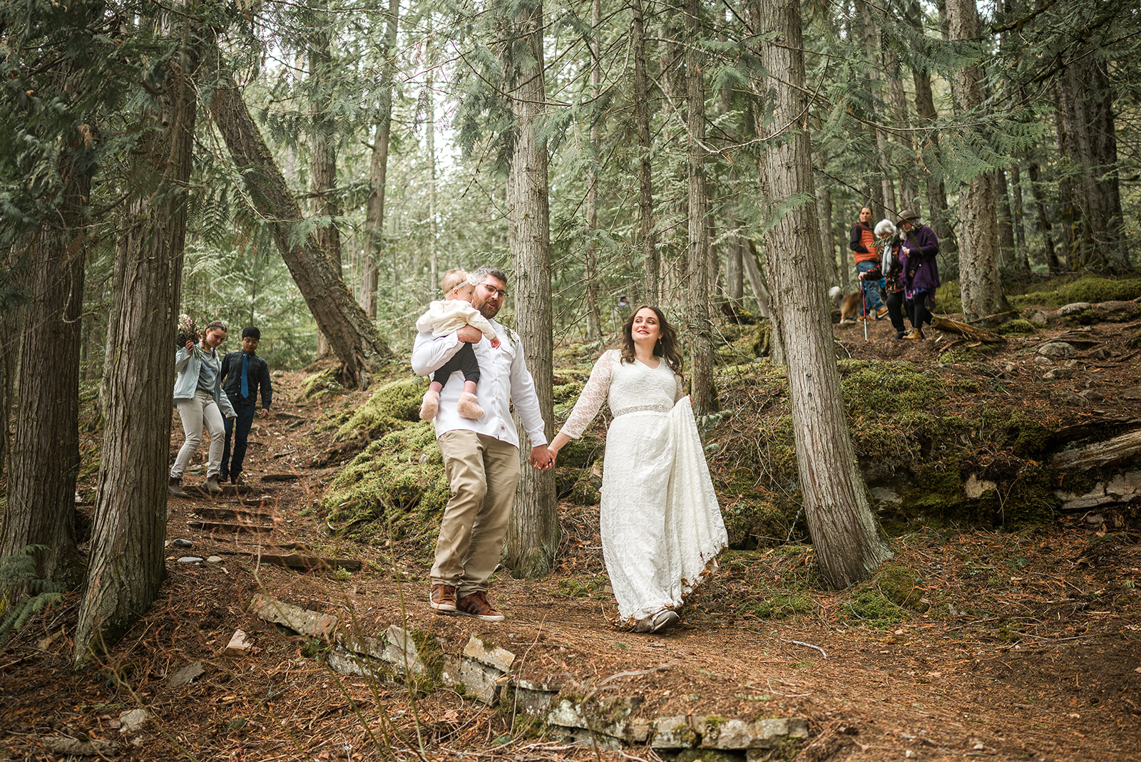 the bride and groom walking down the forest path, guests in the background