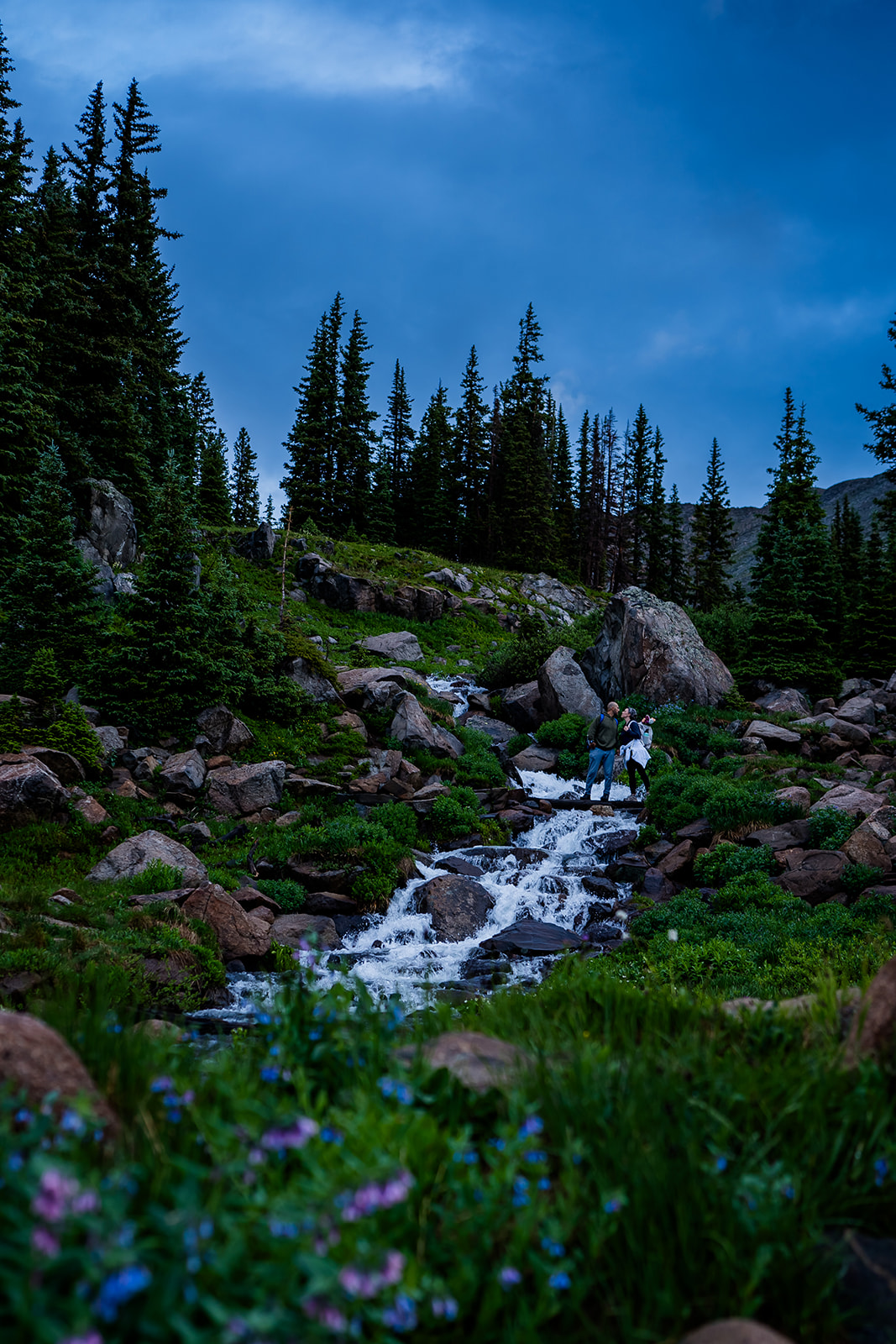 a couple crosses a waterfall on the way to their wild elopement in the Colorado Rocky Mountains