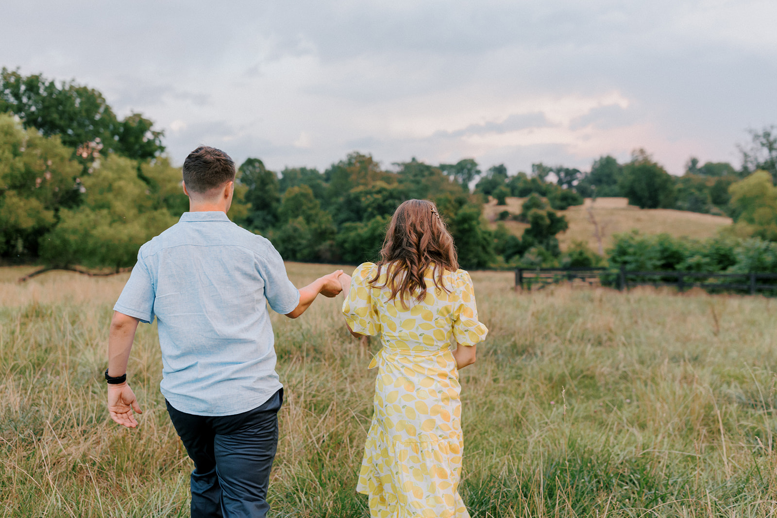 Couple hold hands walking away into a field Warrenton Virginia engagement portraits