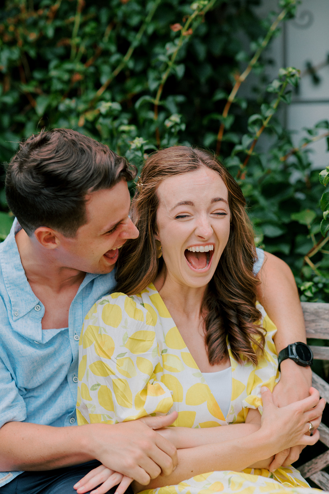 Couple laughs together while sitting on bench in a garden during Virginia engagement photos