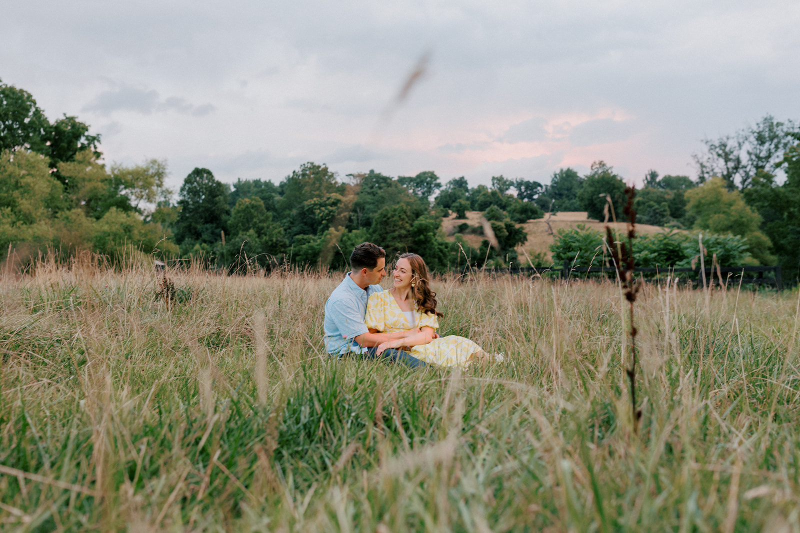 A couple sits in a field at sunset Virginia engagement portraits