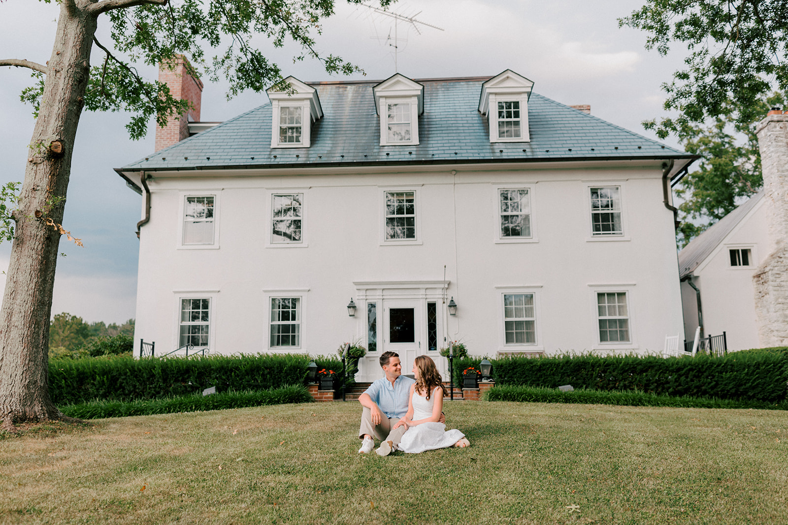 A couple sits in front of large Virginia estate during engagement photos