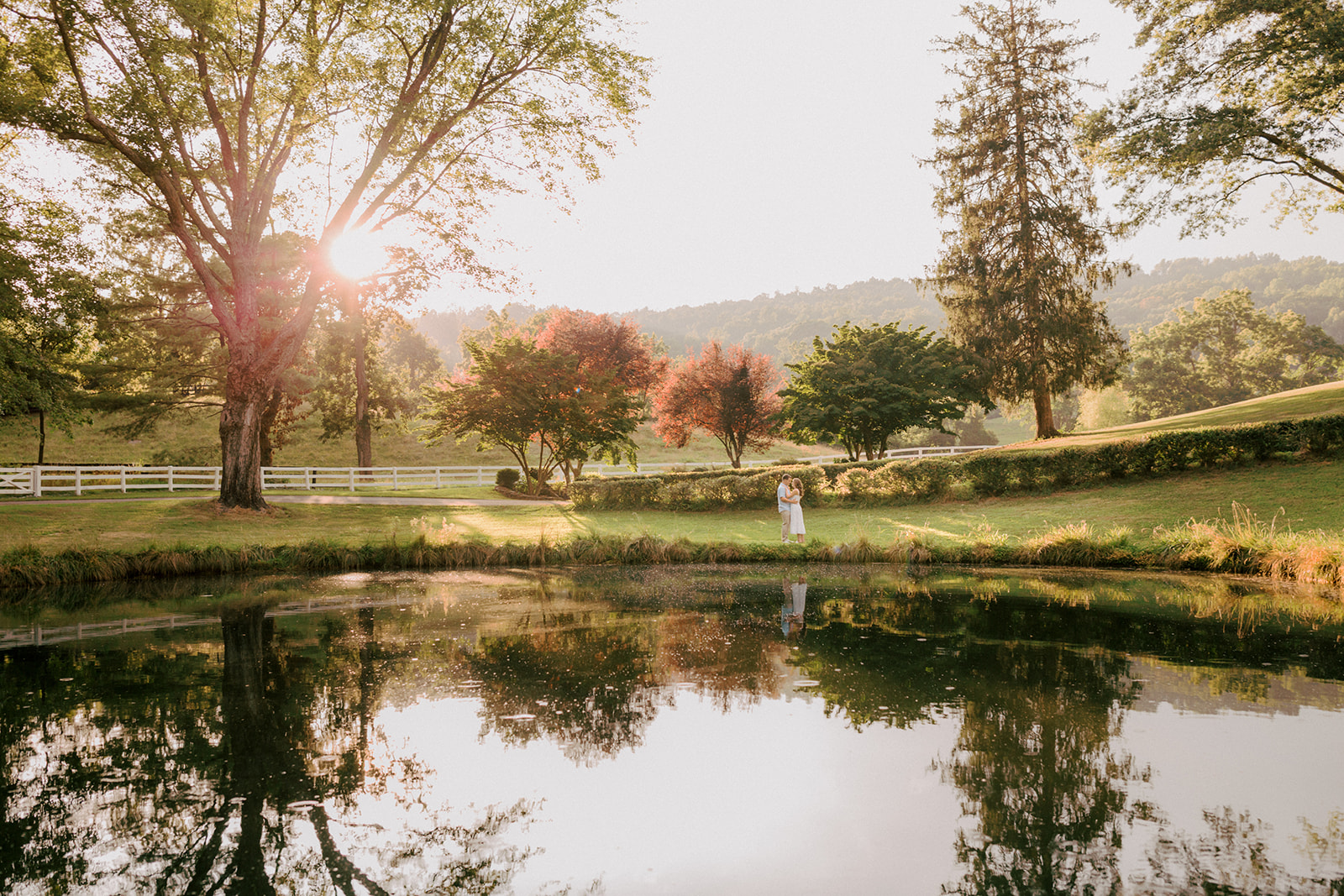 A couple walks across a beautiful pond in Virginia at sunset during engagement photos