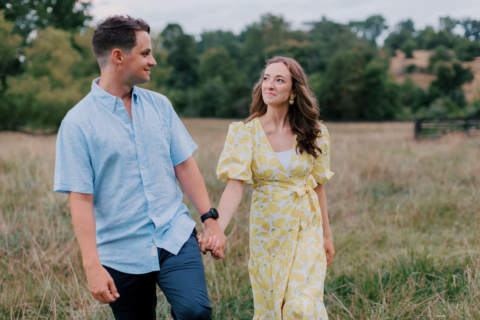 Couple walks through field hand in hand Virginia engagement photos