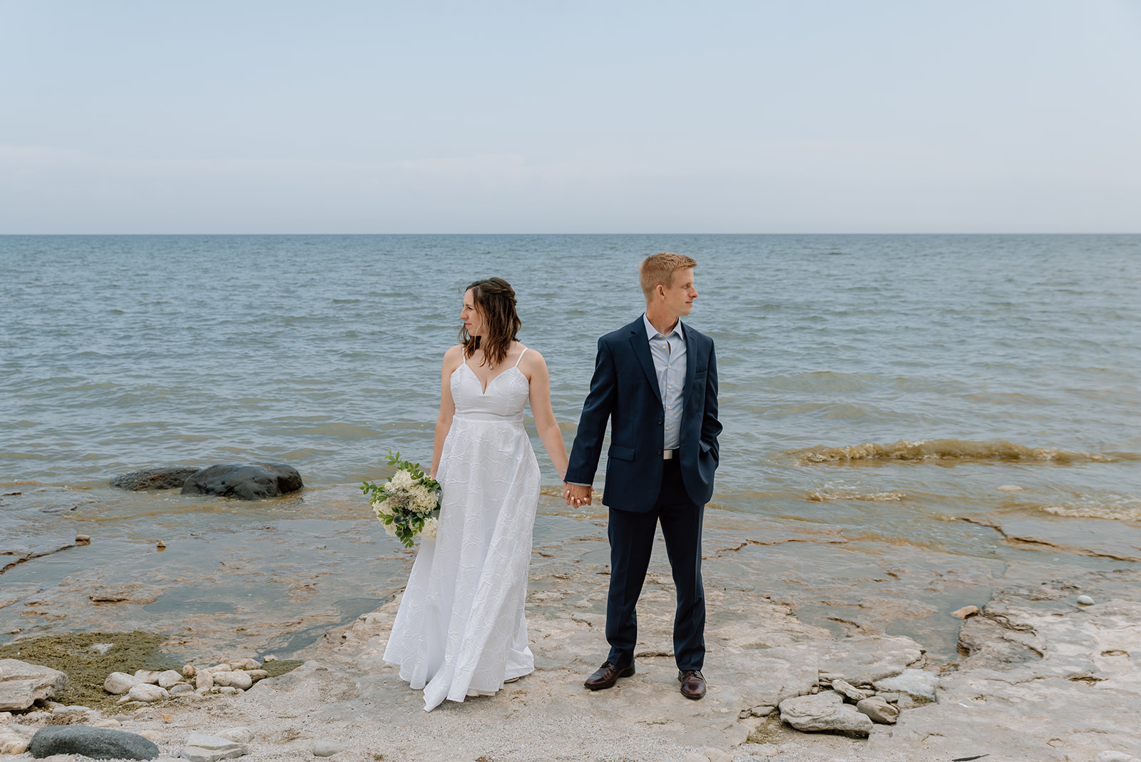 Bride and groom stand along the Lake Michigan shoreline and feel the wind blowing on their faces