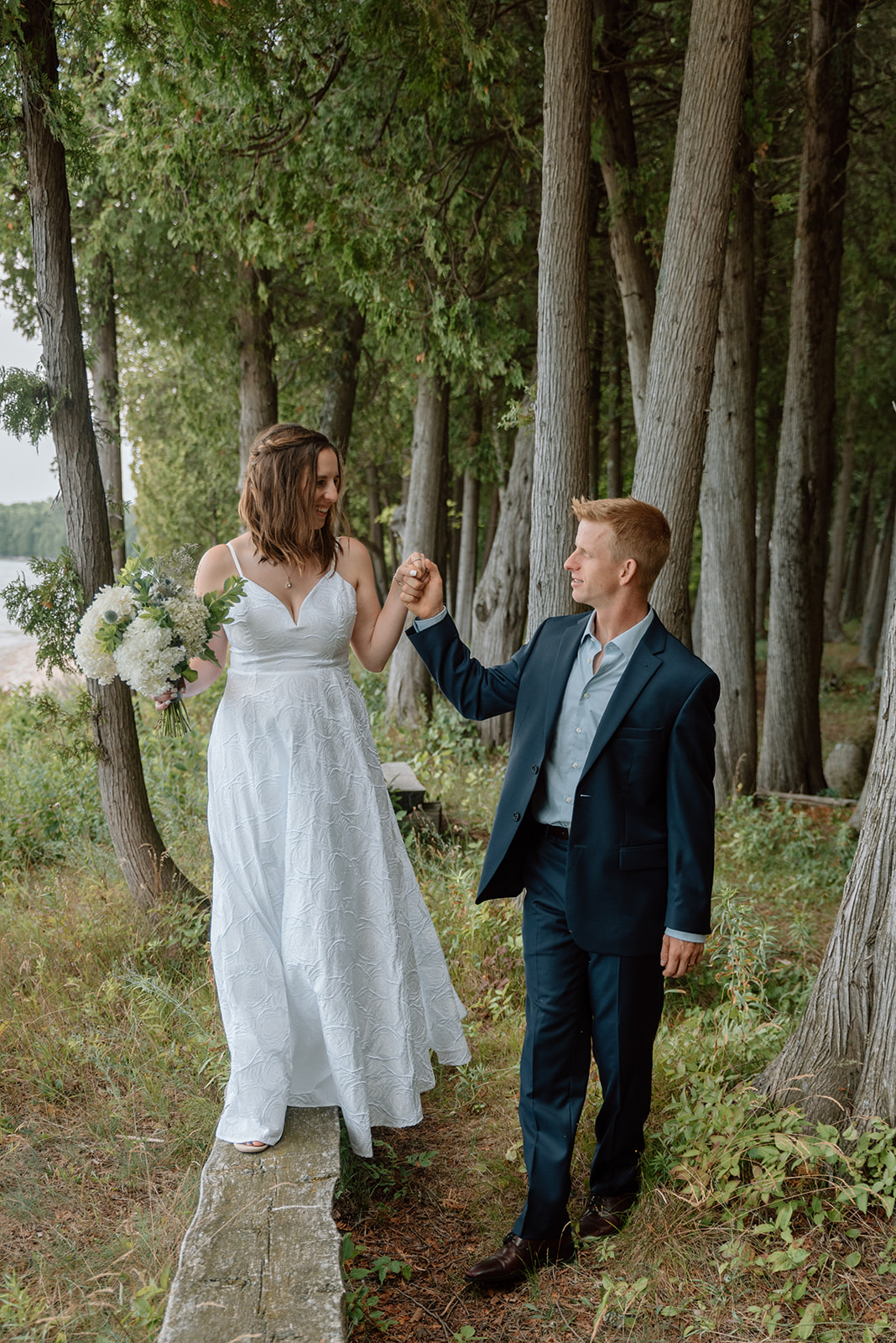Bride walks along bench while holding groom's hand at Bjorklunden