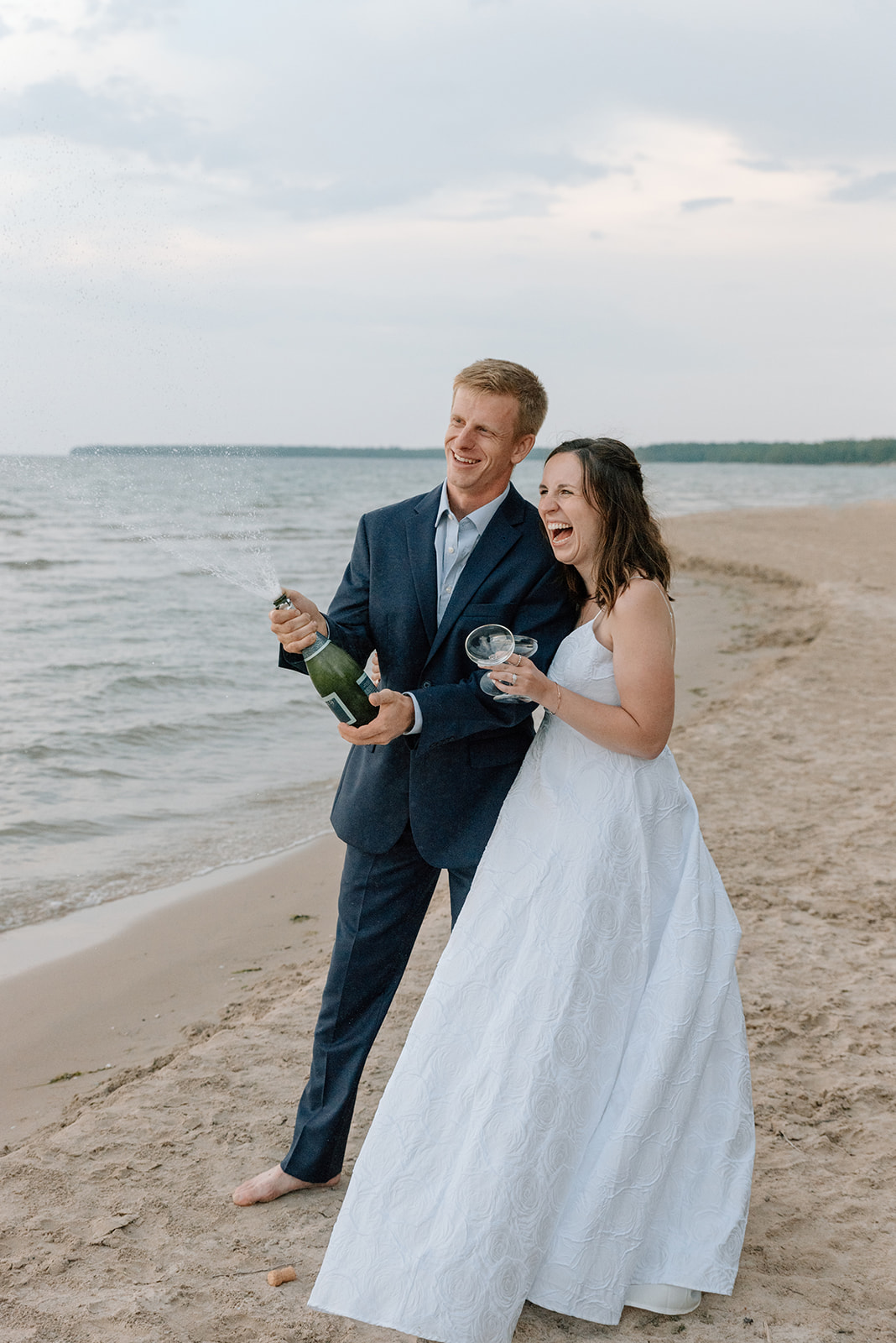 Couple celebrates their vow renewal by popping a bottle of champagne on the beach