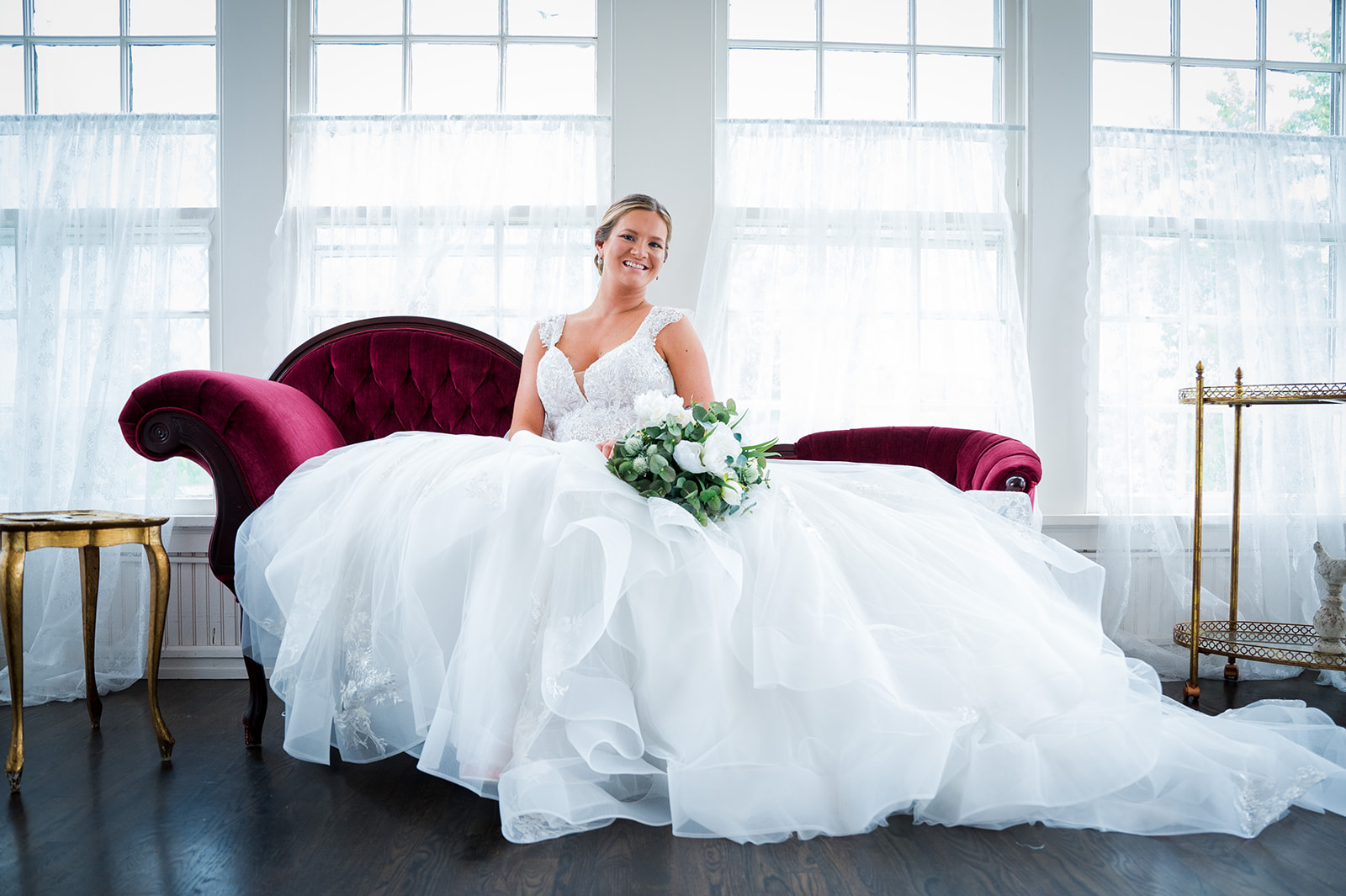 Bride sits on a red velvet couch in her wedding dress.