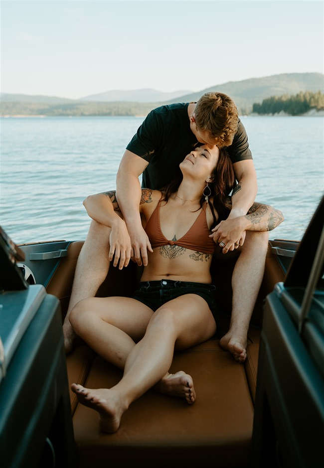 couple snuggled up on their malibu boat at sunset for adventurous lake engagement photos