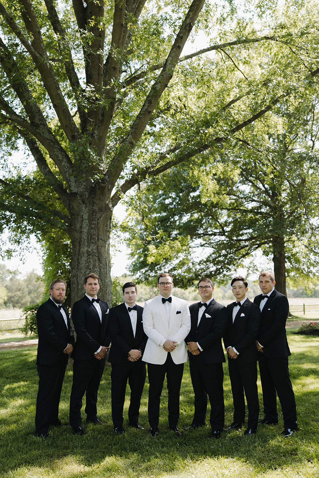 groom stands beside groomsmen at outdoor wedding 