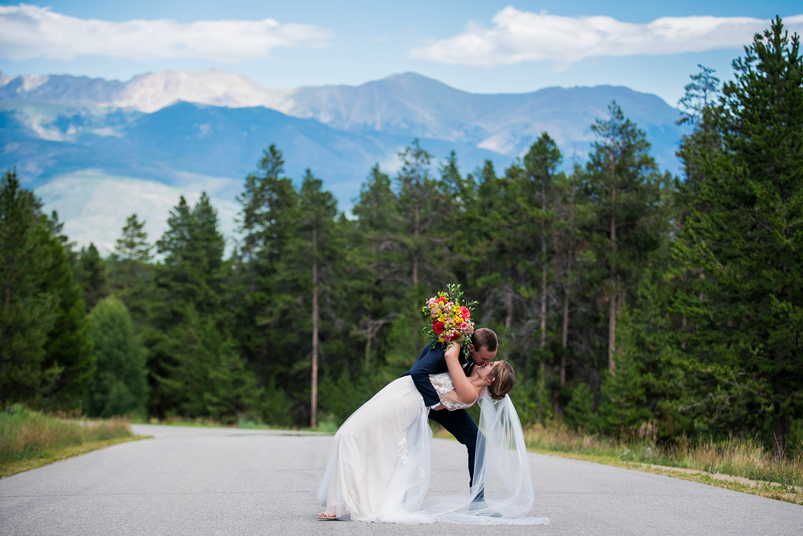 The groom dips the bride for a kiss with the Colorado Rocky Mountains in the background.