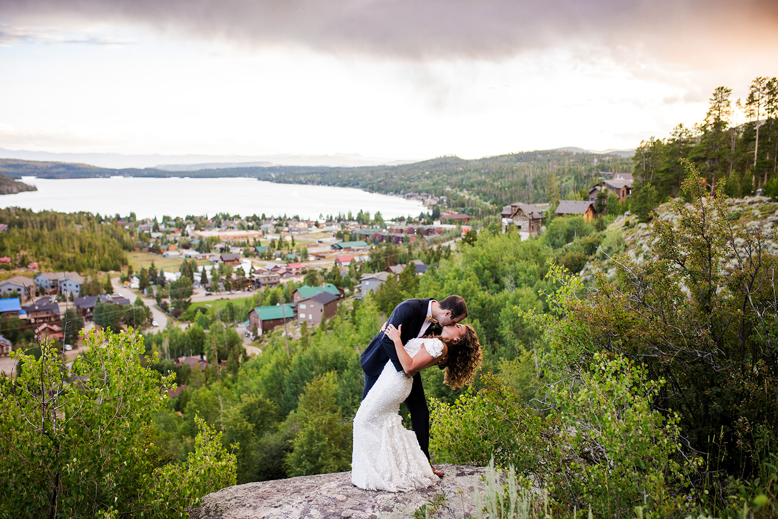 Groom dips bride for a kiss at golden hour with views of Grand Lake in the background.
