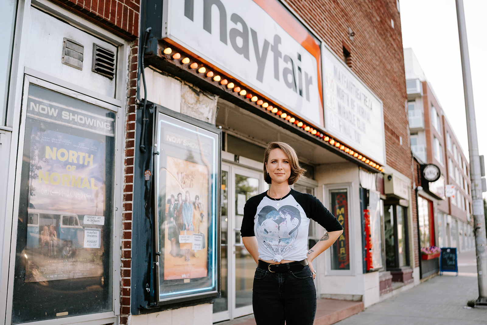 a woman standing in front of the Mayfair Theatre in Ottawa, Ontario, Canada while smiling