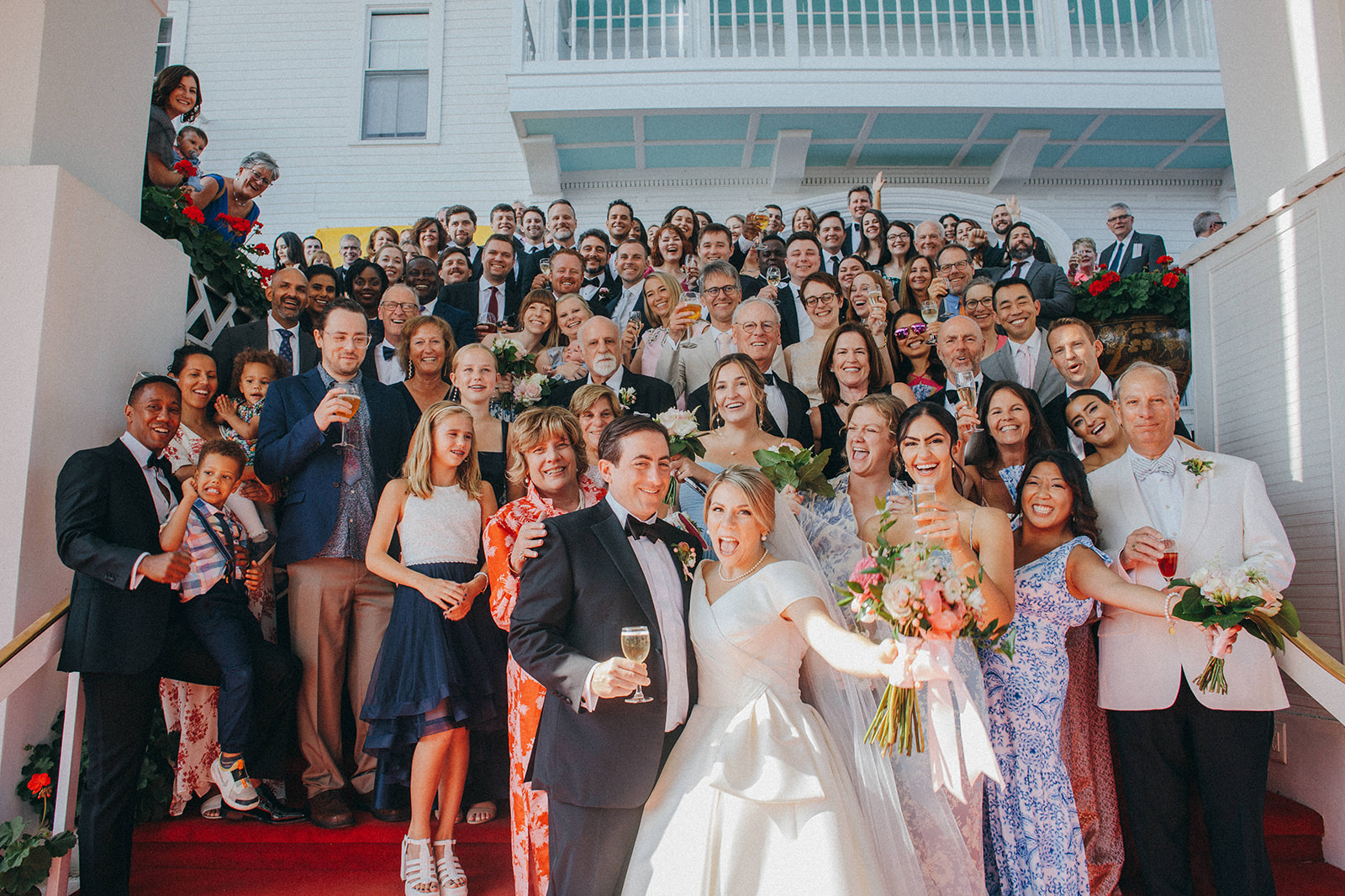 A bride and groom get a photo with all their wedding guests on the red carpeted steps at the Grand Hotel