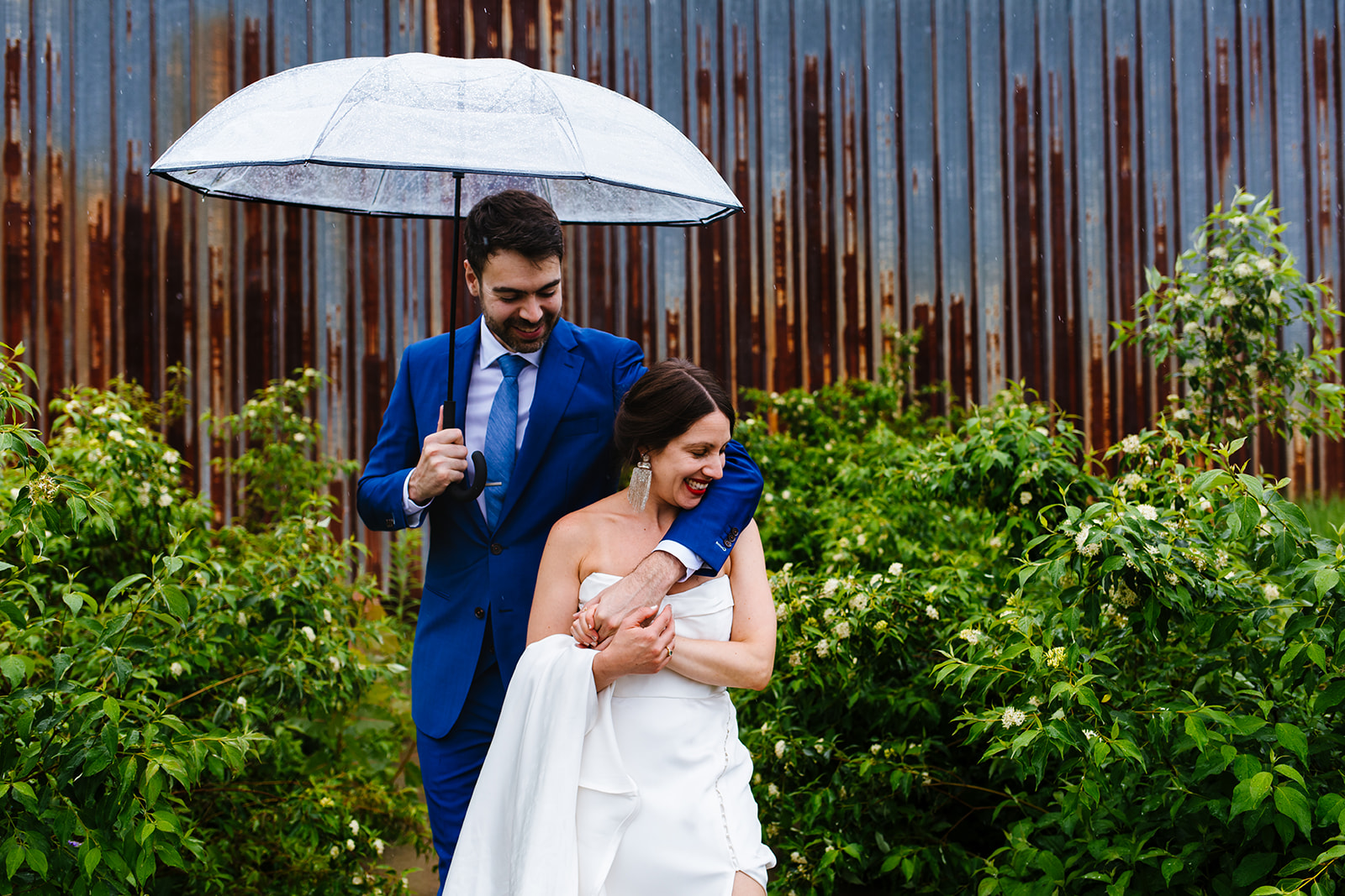 Bride and groom pose under an umbrella during their rainy wedding day at Greylock Works