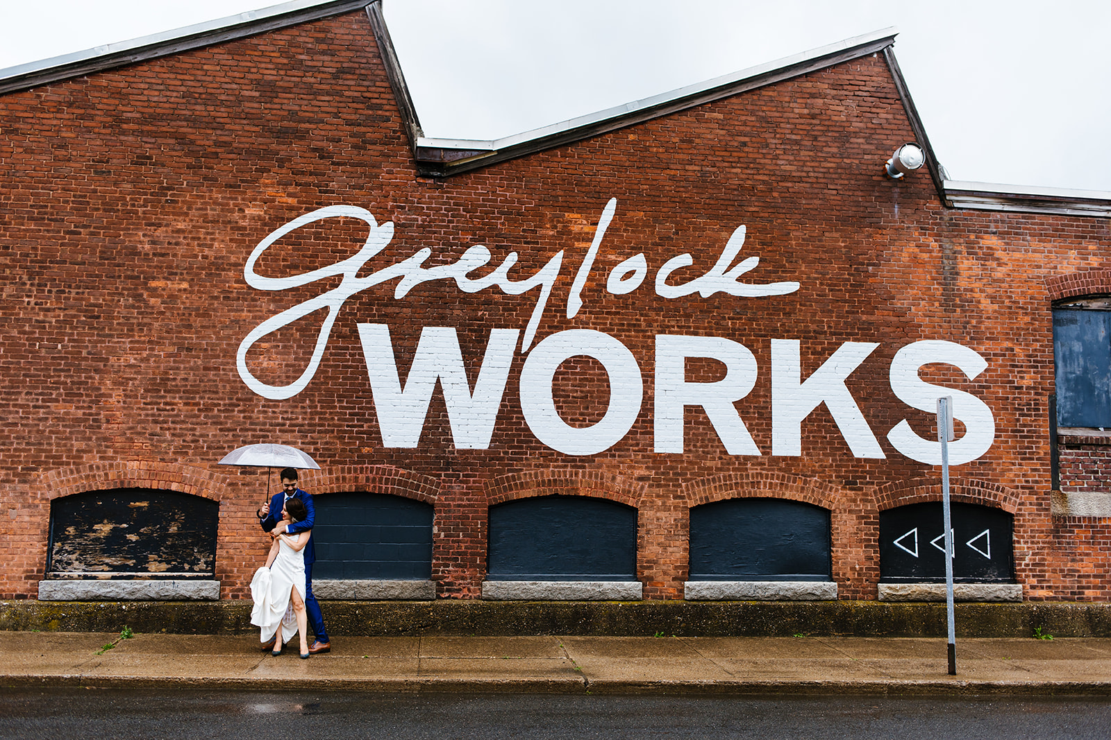 Bride and groom pose in front of a building that says Grelock Works on it.