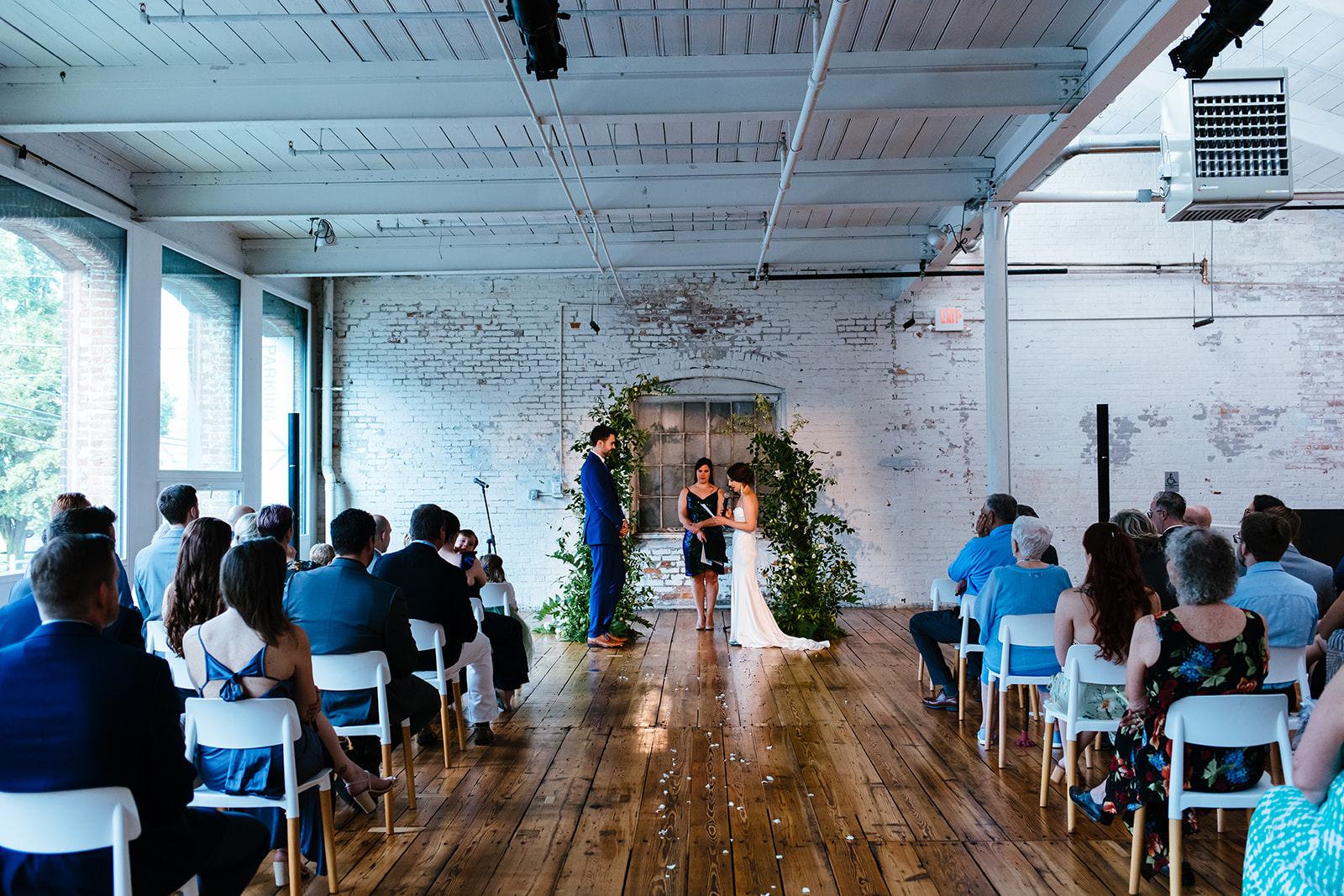 Bride and groom stand under an arch of greenery inside Greylock Works during their wedding ceremony