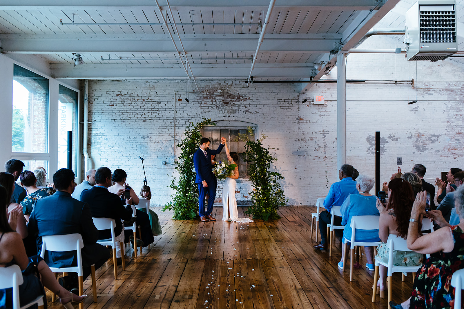 Bride and groom stand under an arch of greenery inside Greylock Works during their wedding ceremony