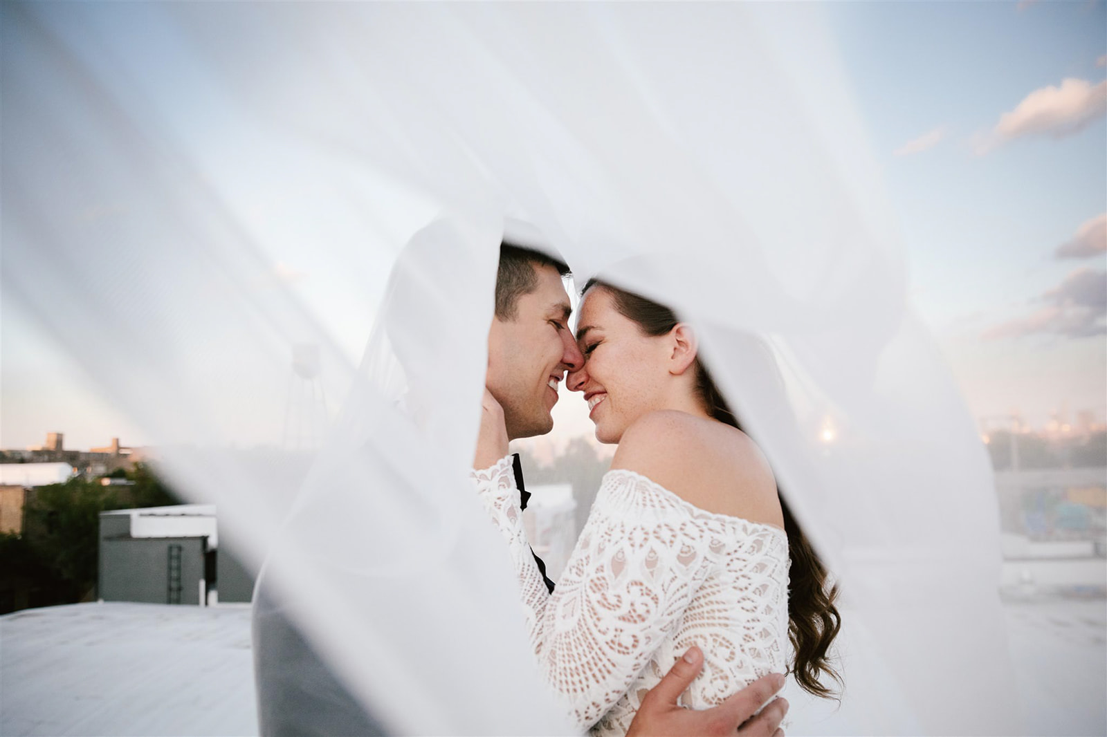 Bride's veil dances in the sunset breeze as she embraces her groom on Walden Chicago rooftop.