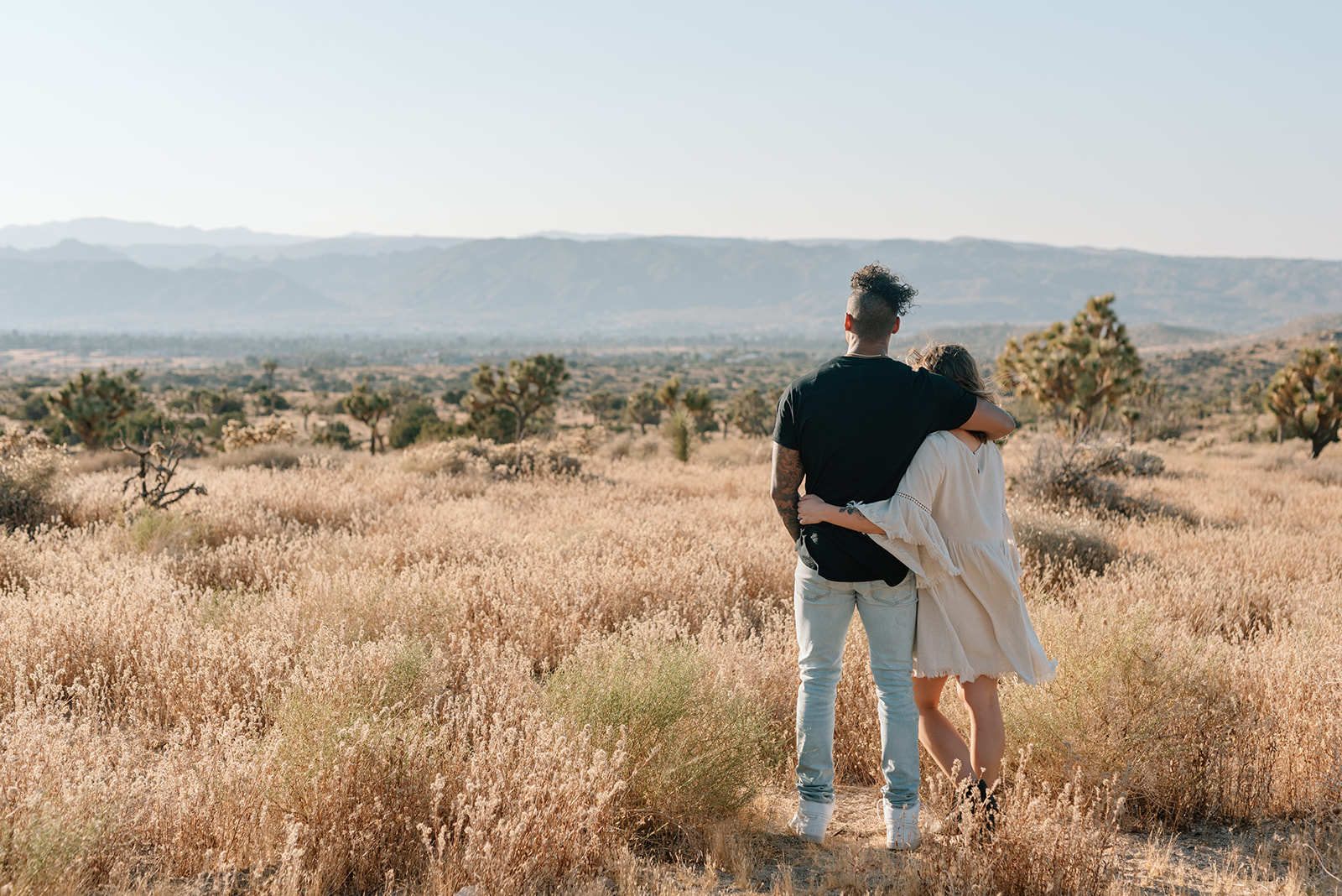 Engaged couple wraps their arms around each other and gazes out at the mountains in Southern California