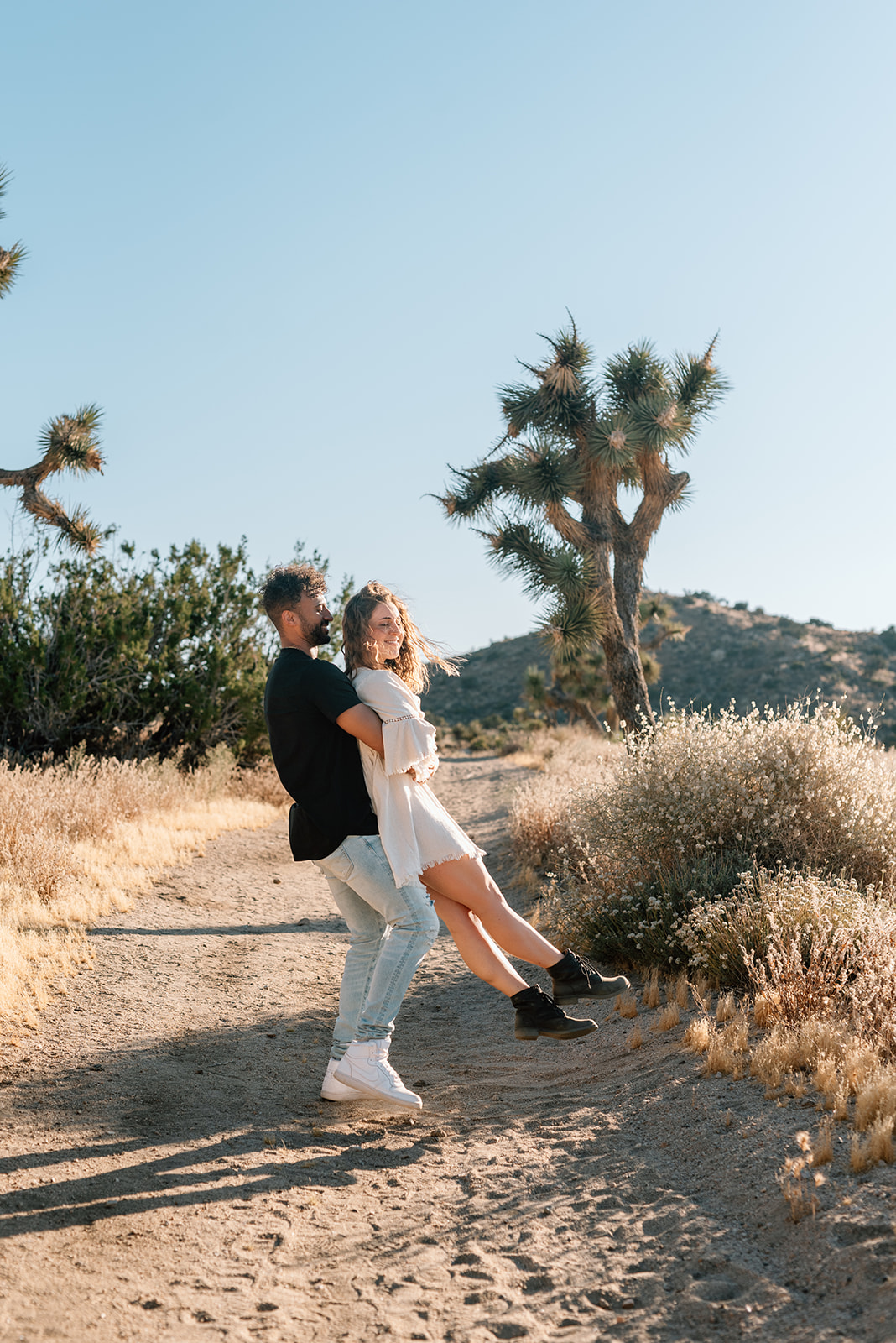 Engaged man picks up his fiance and spins her in the desert with mountains and cacti in the background