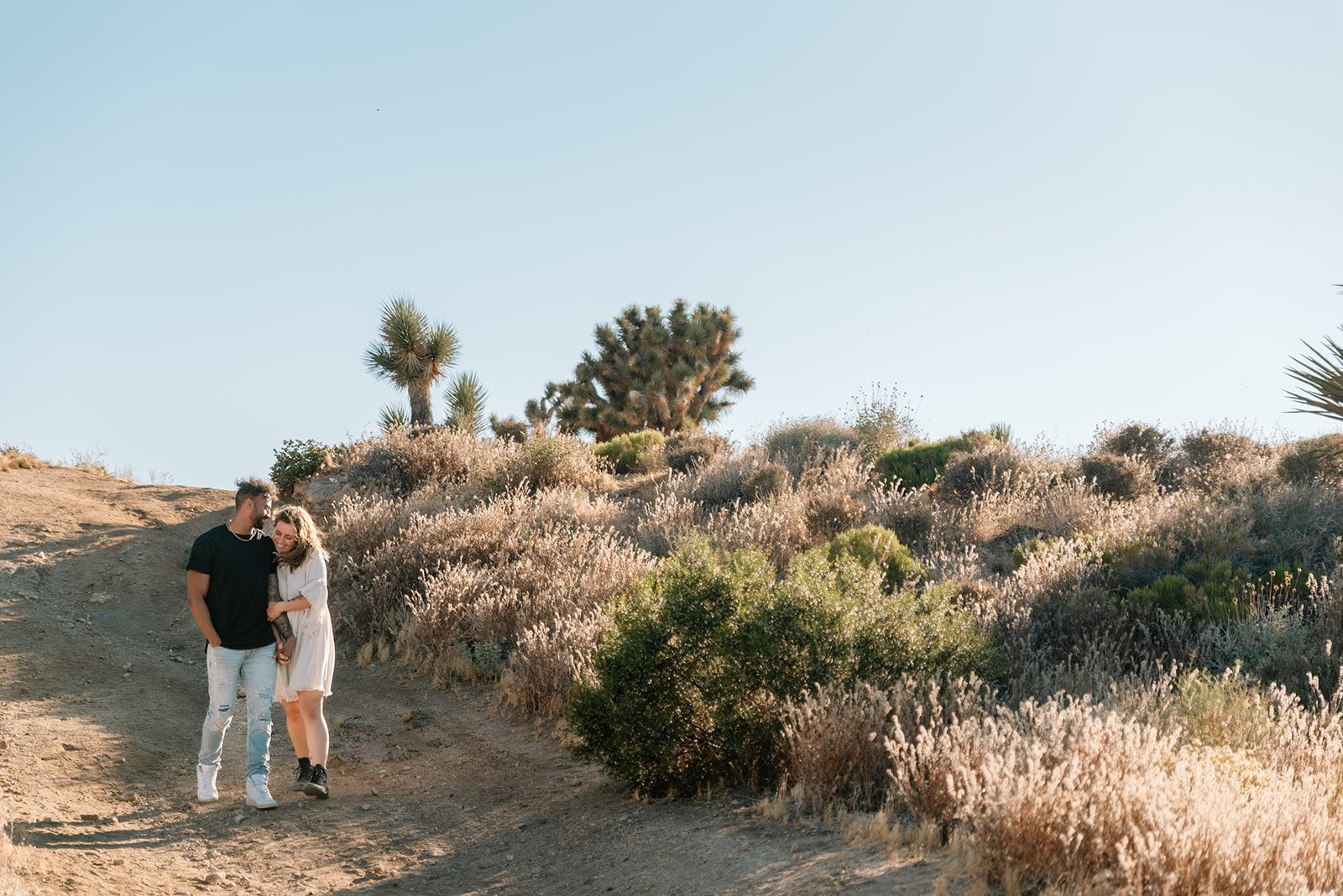 Man and woman snuggle and walk down dusty desert path together