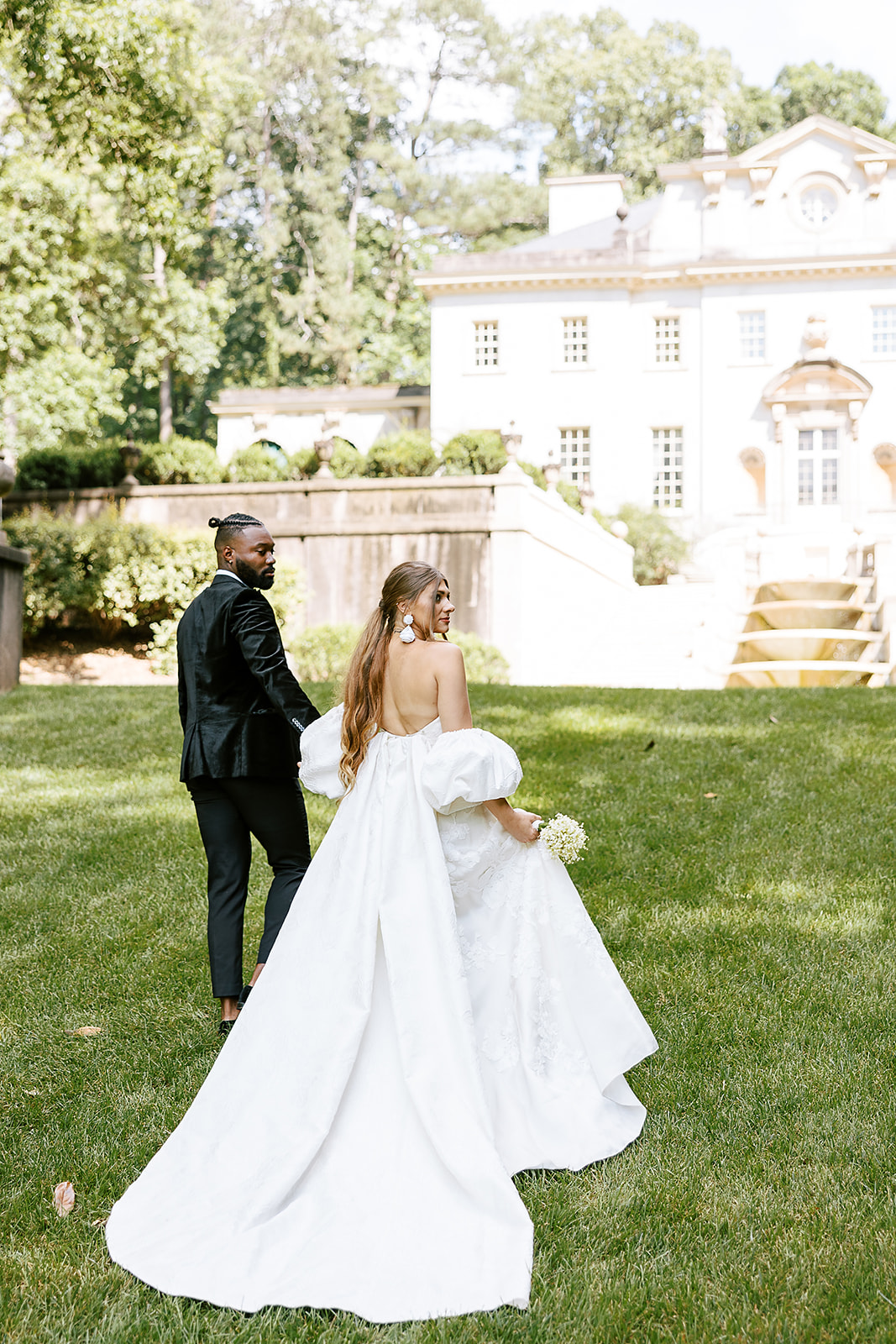 A SWAN HOUSE ANNIVERSARY EDITORIAL IN ATLANTA, GA SHOT OF BRIDE. ANDGROOM WALKING ON THE LAWN WITH WATERFALL IN THE BACK