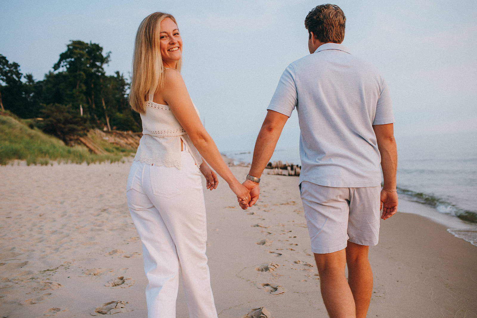Genuine and fun engaged couple walks down the beach of Lake Michigan near Grand Haven