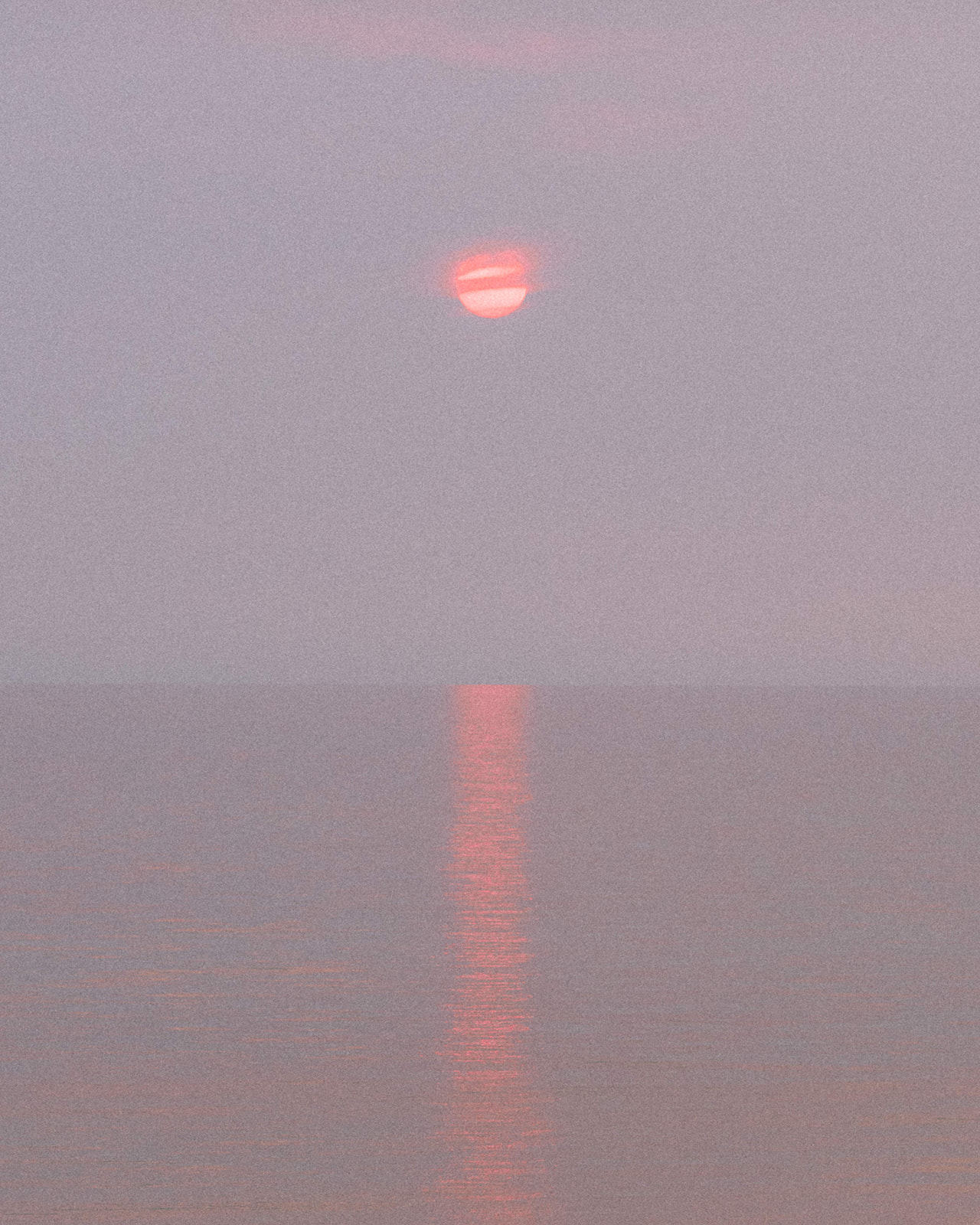 A hazy red and orange sunset reflecting off the still and calm waters of Lake Michigan