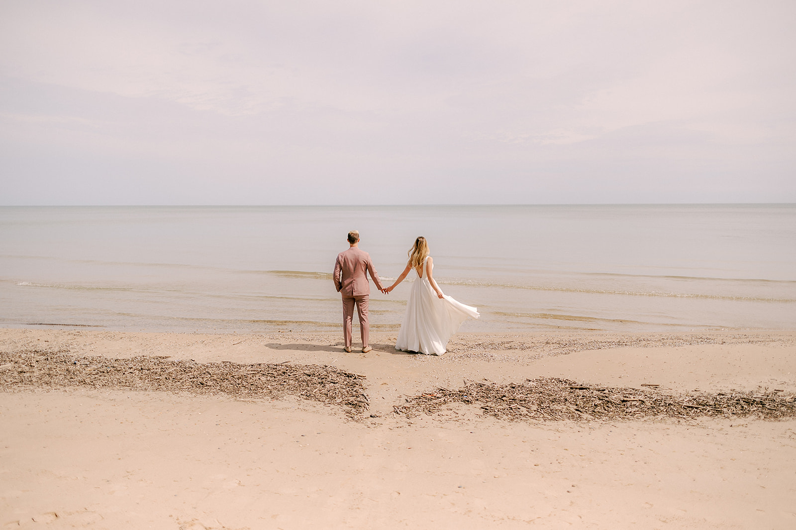 bride and groom hold hands on the shore of Lake Michigan during their wedding celebration in Milwaukee