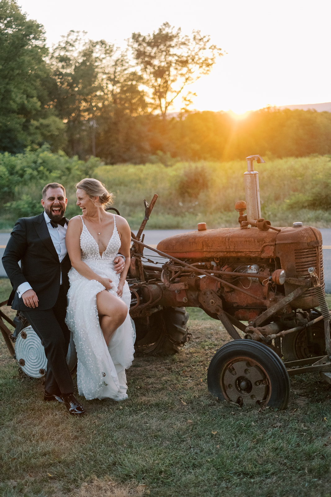 Bride and groom laugh during sunset portraits by a tractor at Virginia barn wedding