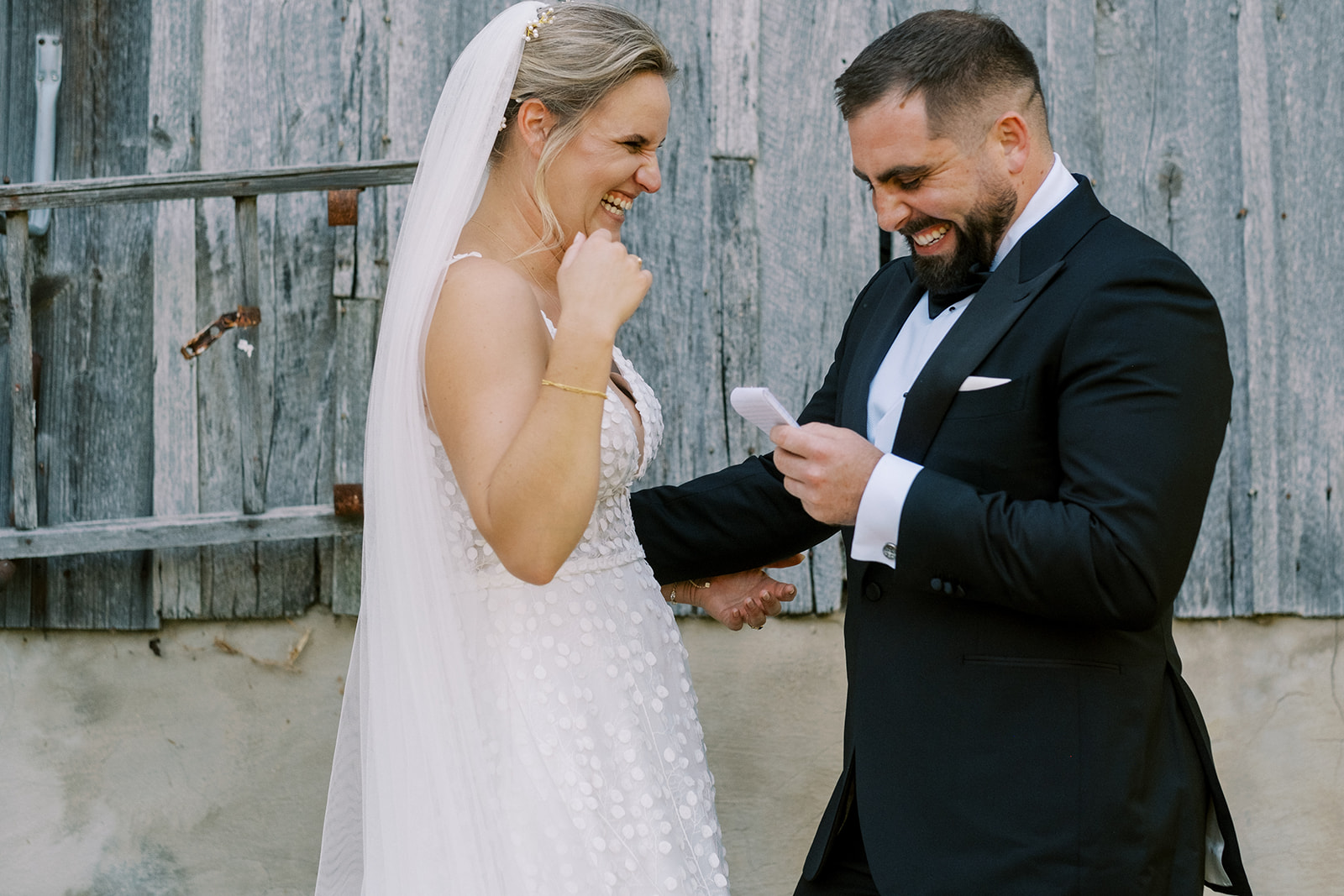 Bride and groom laugh together as groom reads private first vows at Virginia barn wedding