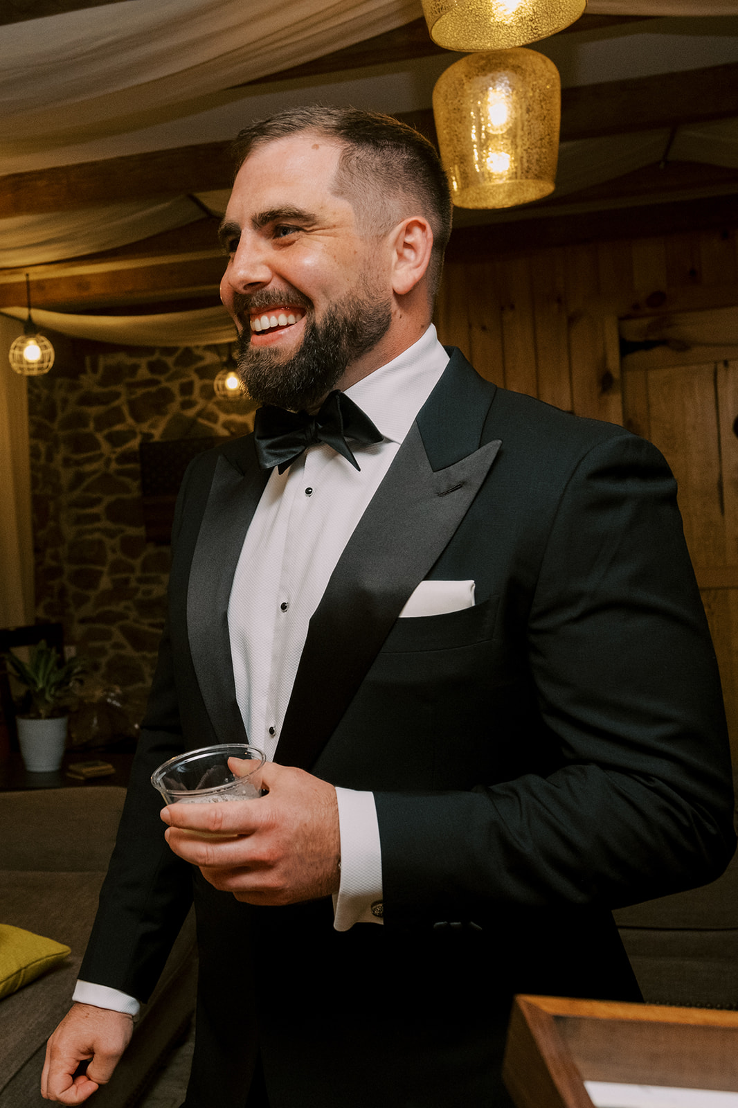 Groom smiles with drink in hand while getting ready at Virginia wedding