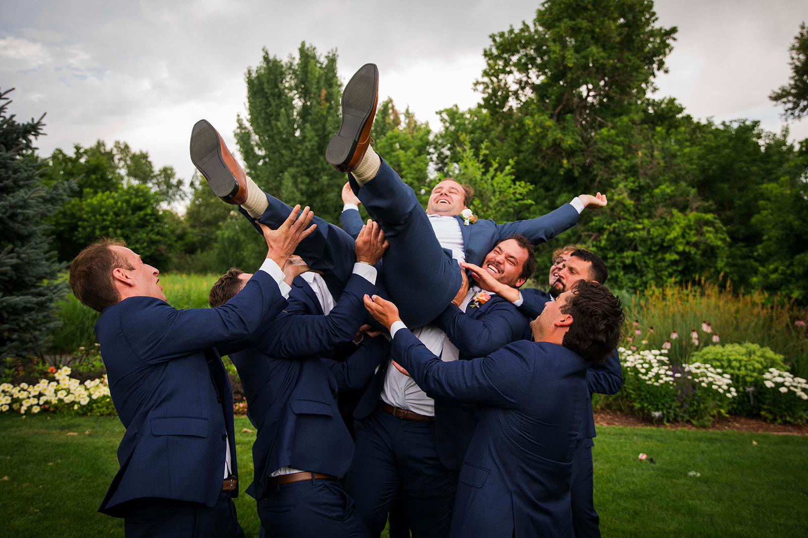 Groomsmen lift groom in the air as they all laugh.